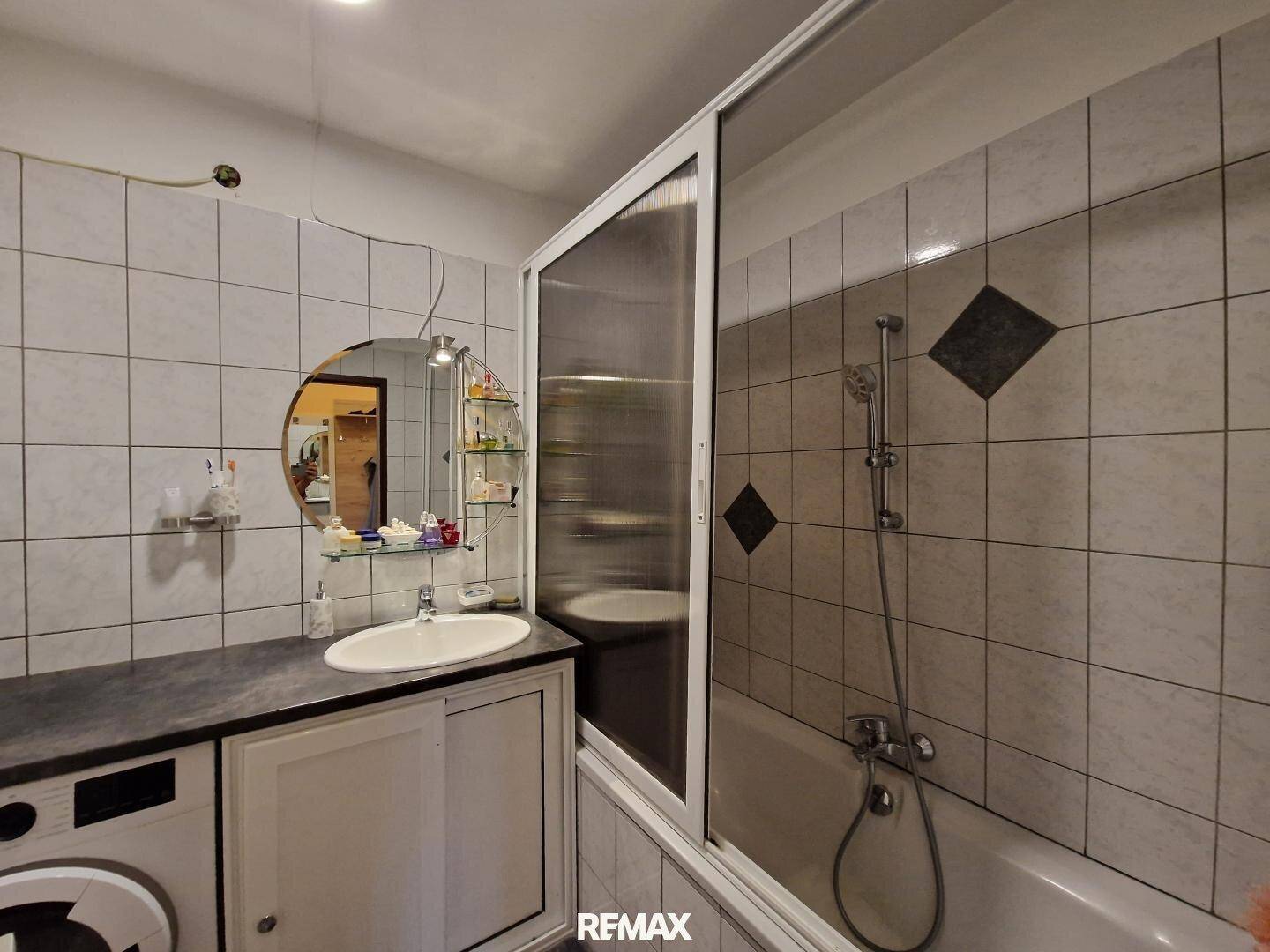 Gefliestes Badezimmer mit Badewanne, Duschabtrennung und Waschbecken.