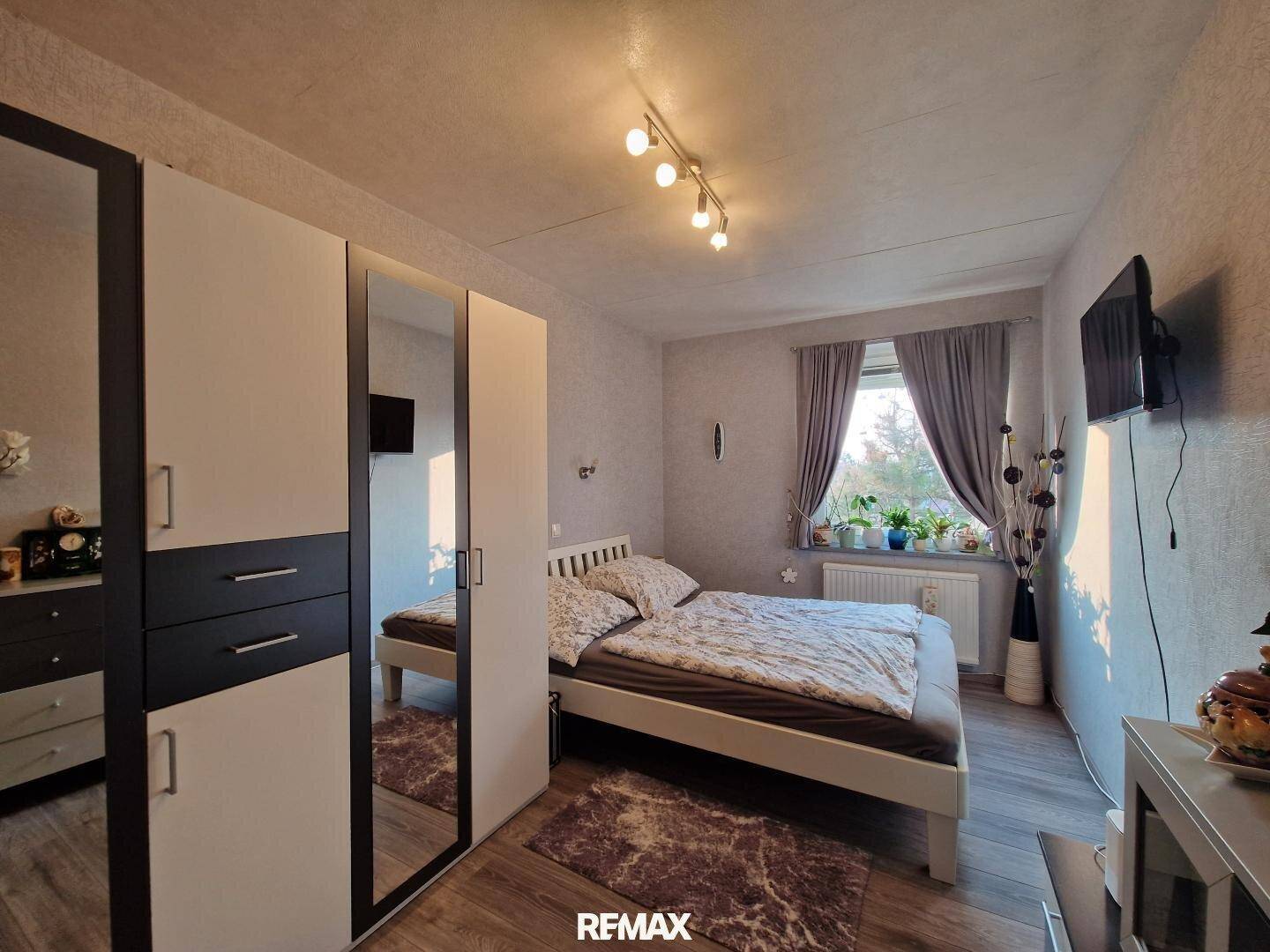 Gemütliches Schlafzimmer mit Doppelbett, Kleiderschrank und Fenster mit Vorhängen.