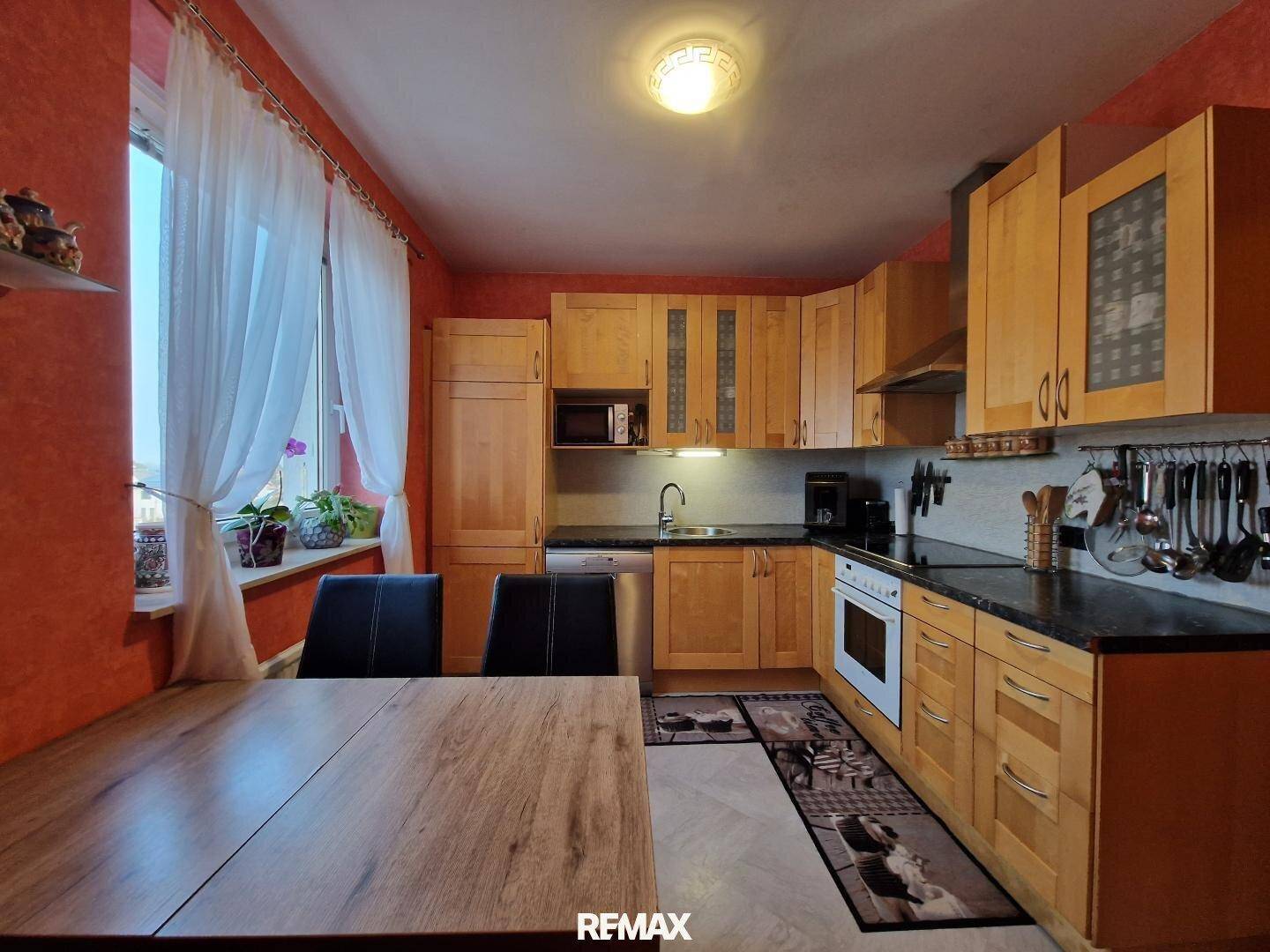 Funktionale Küche mit Holzschränken, Essbereich und Fenster für Tageslicht.