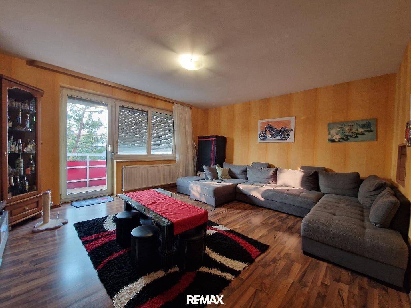 Geräumiges Wohnzimmer mit großem Sofa, Laminatboden und Zugang zum Balkon.