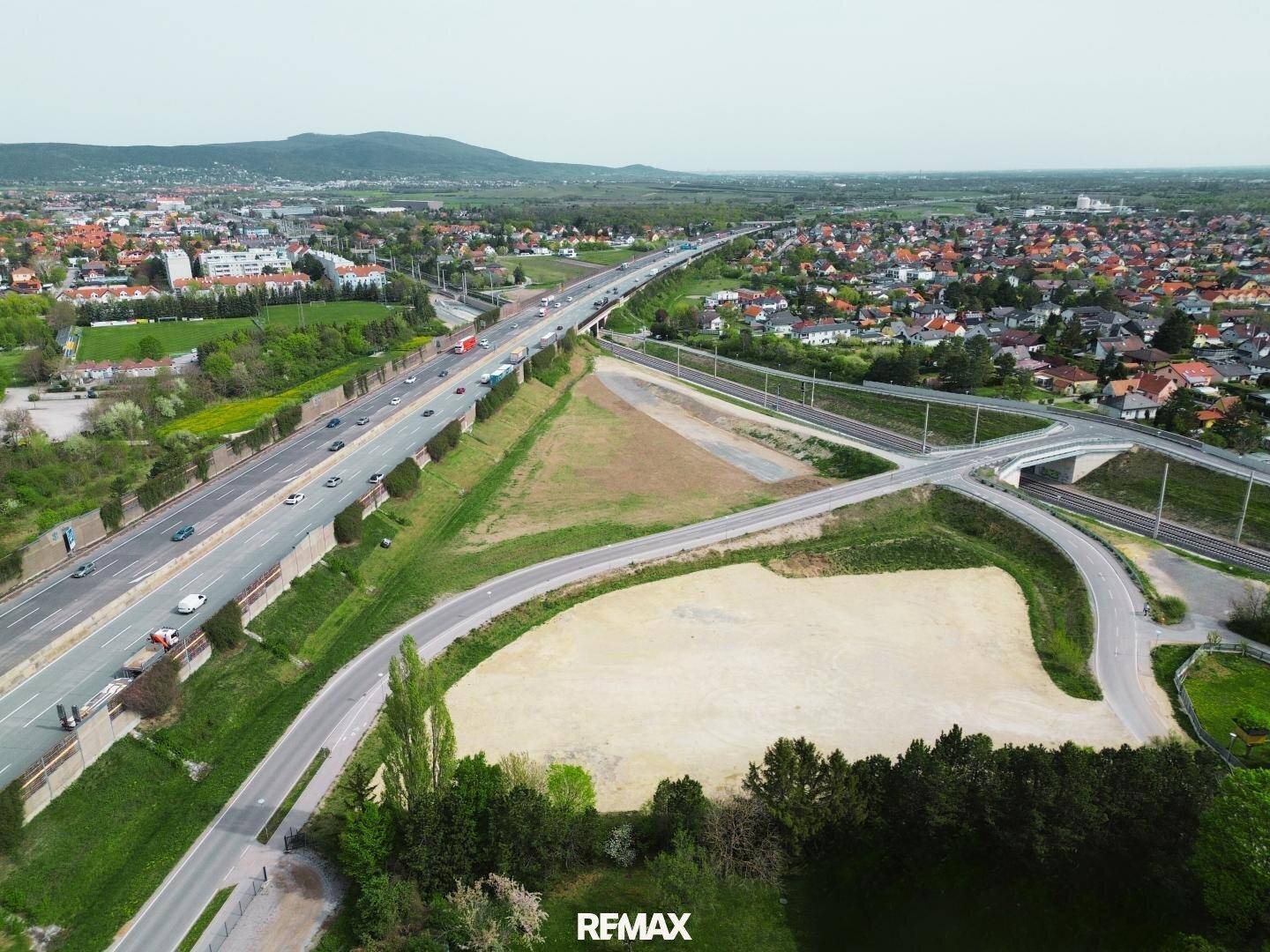Panoramische Luftaufnahme eines Grundstücks mit Autobahnkreuz, umliegender Stadt und Hügellandschaft.