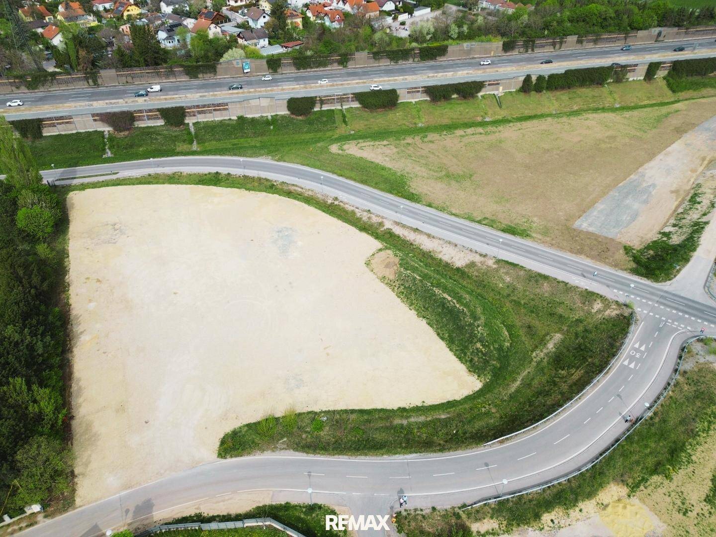Weitläufige Luftaufnahme eines Baugrundstücks mit angrenzender Straße und Autobahn im Hintergrund.
