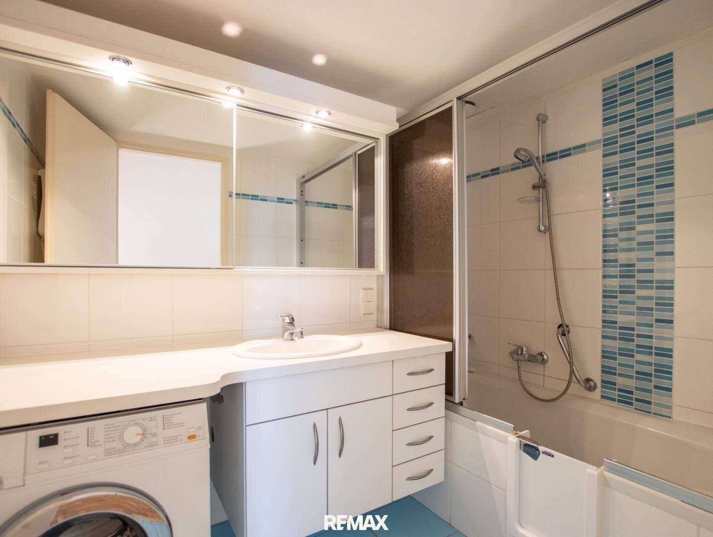 Badezimmer mit Badewanne, Duschabtrennung, Waschbecken und Waschmaschine.