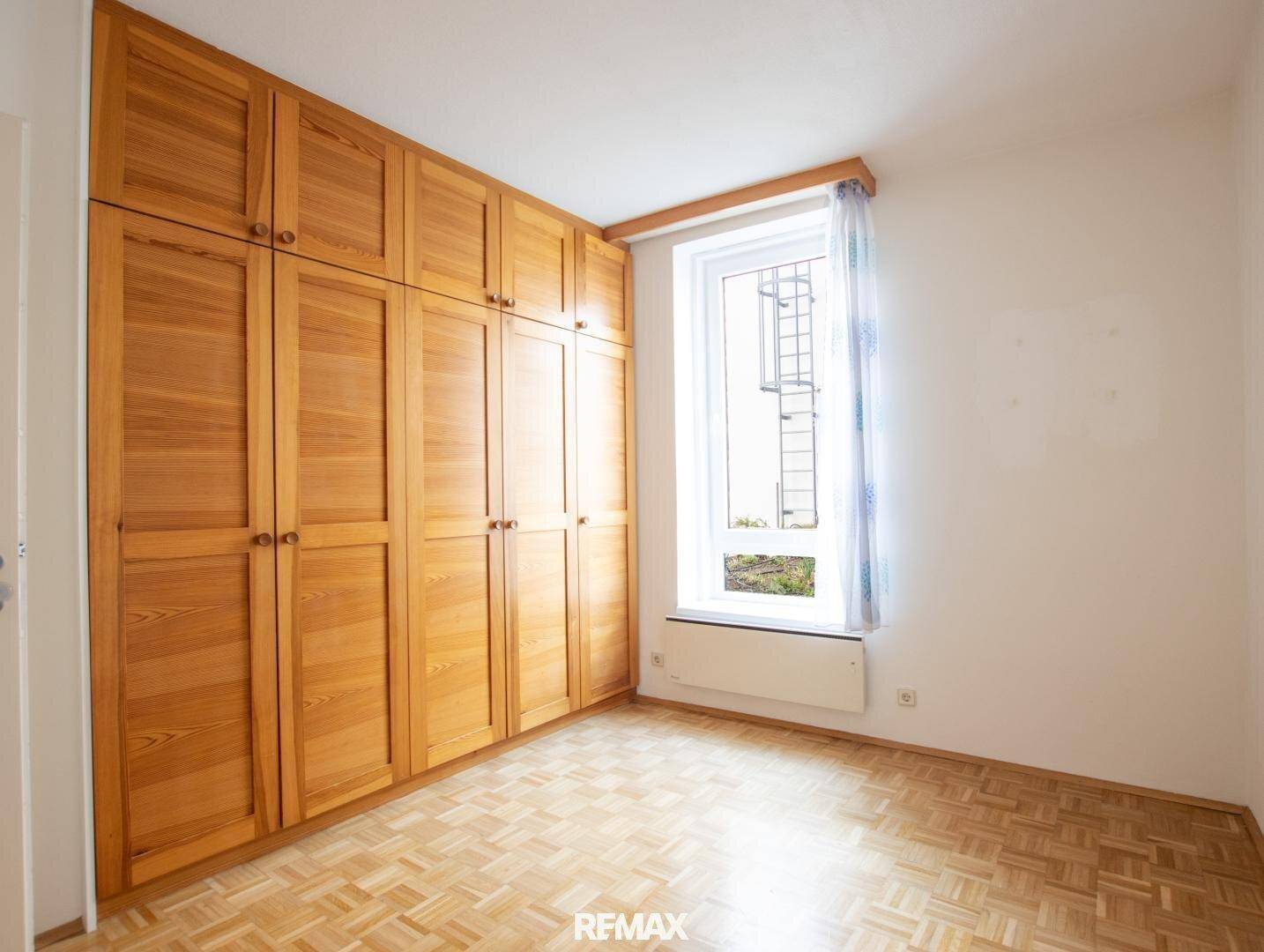 Schlafzimmer mit integriertem Holzschrank und Parkettboden, bietet viel Stauraum.