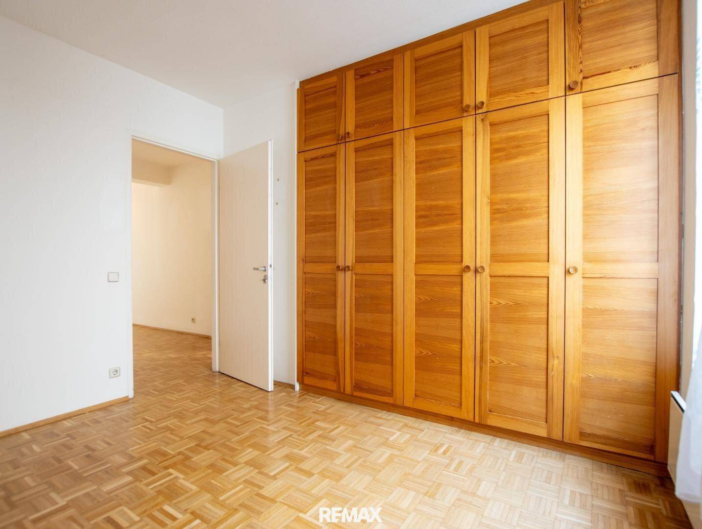 Geräumiges Zimmer mit großen Holzschränken und Zugang zu einem weiteren Raum.