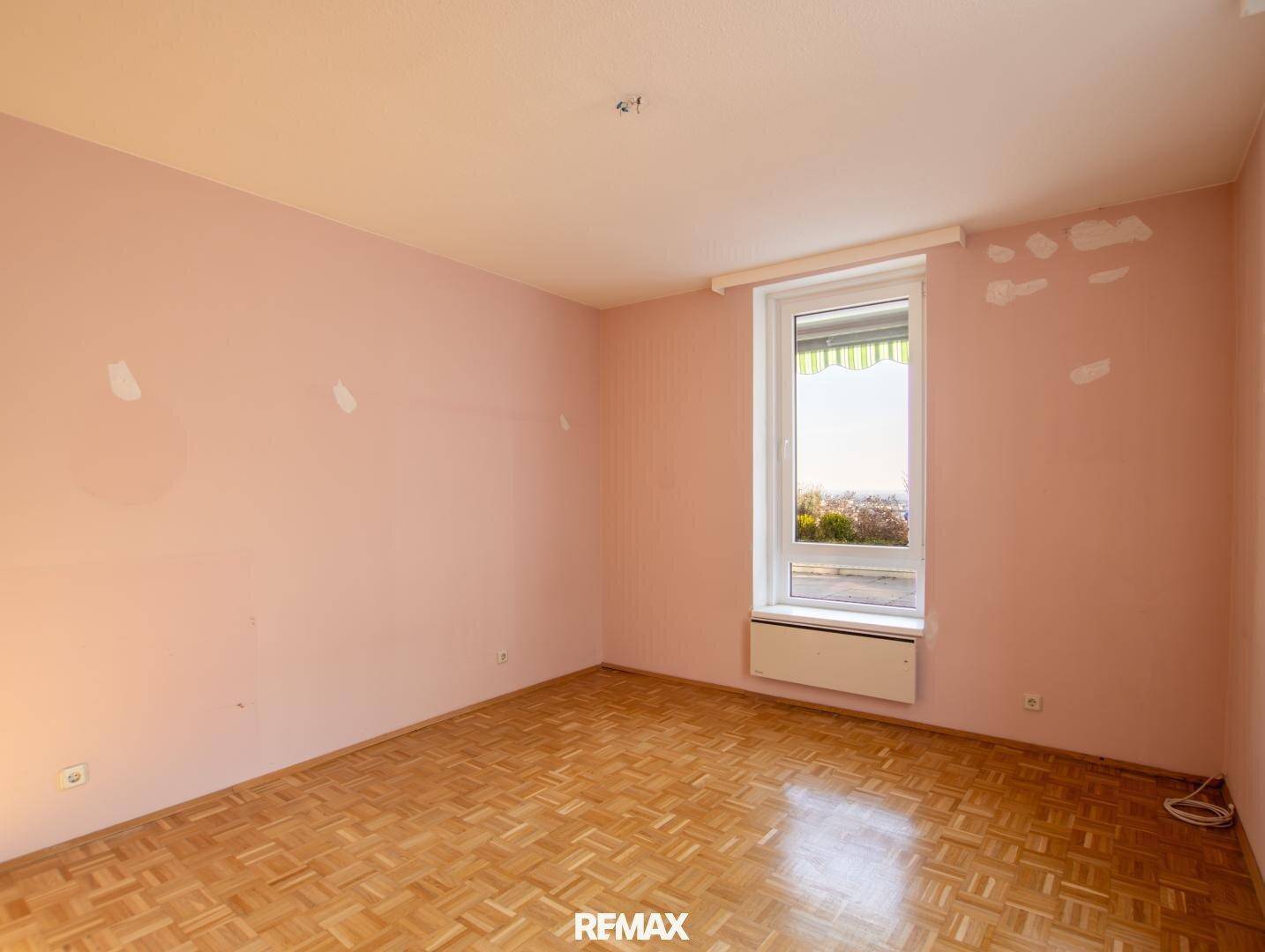 Leeres Schlafzimmer mit Parkettboden und rosa Wänden, bereit zur individuellen Gestaltung.