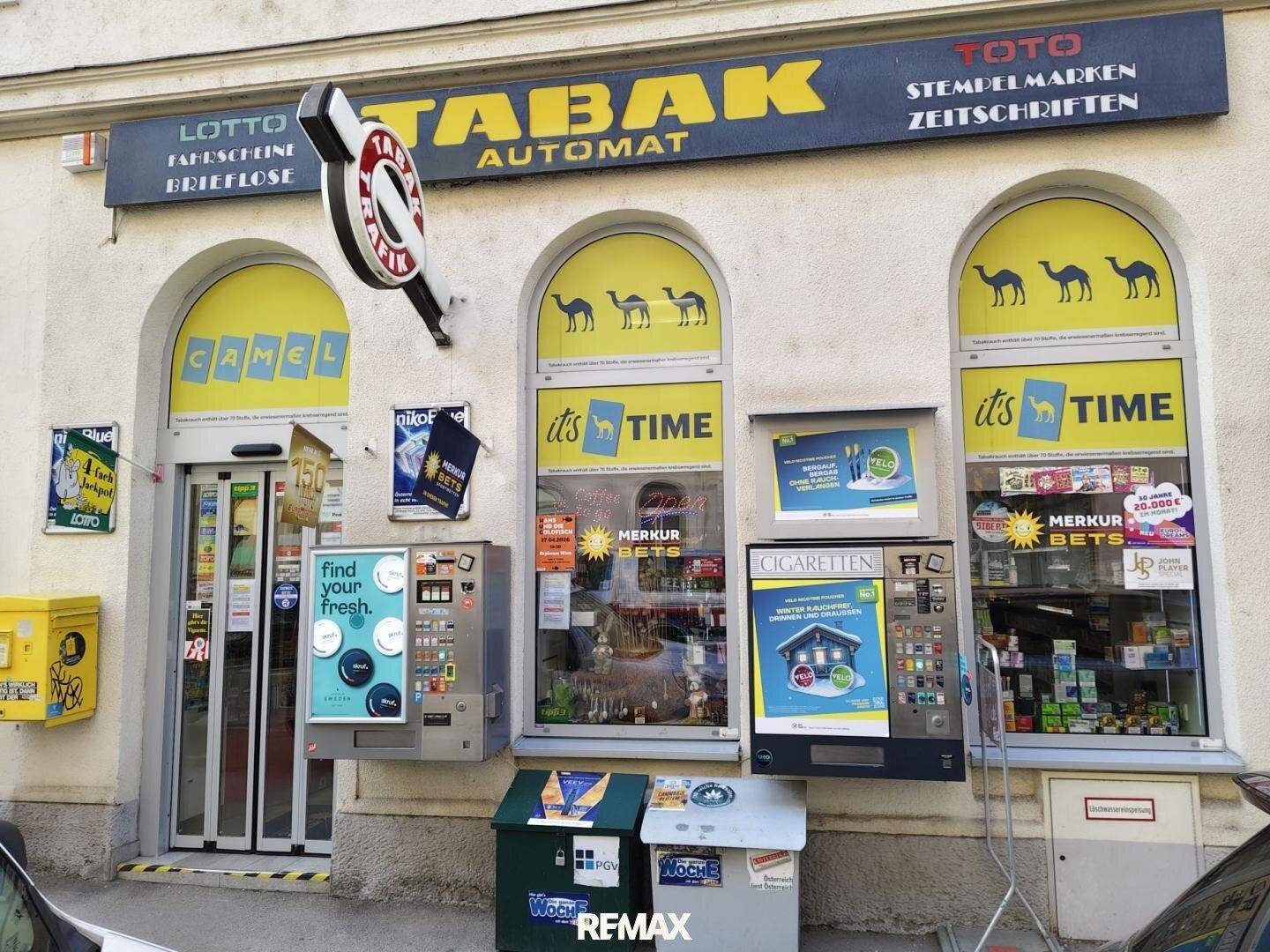 Außenansicht eines Tabakladens mit gelben Akzenten, Automaten und einem großen Schild.