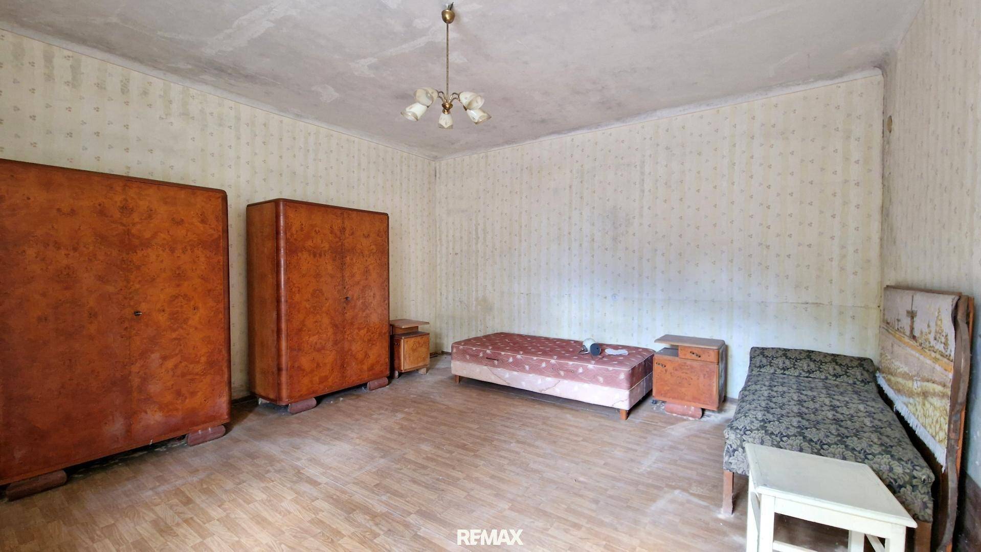 Schlafzimmer im Originalzustand mit zwei Betten, Holzschränken und einfacher Deckenleuchte.