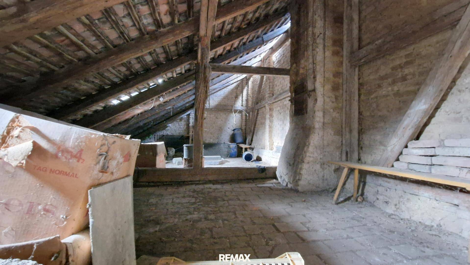 Geräumiger Dachboden mit sichtbaren Holzbalken, Ziegelwänden und viel Potenzial zur Renovierung.
