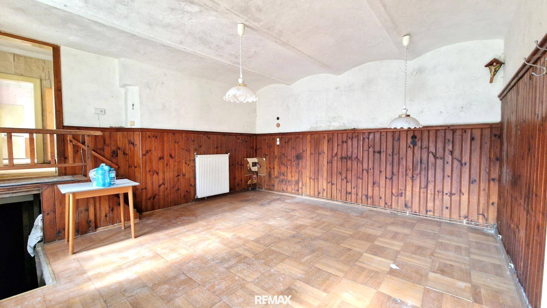 Wohnraum mit dunkler Holzvertäfelung, kariertem Boden und einem Heizkörper unter dem Fenster.