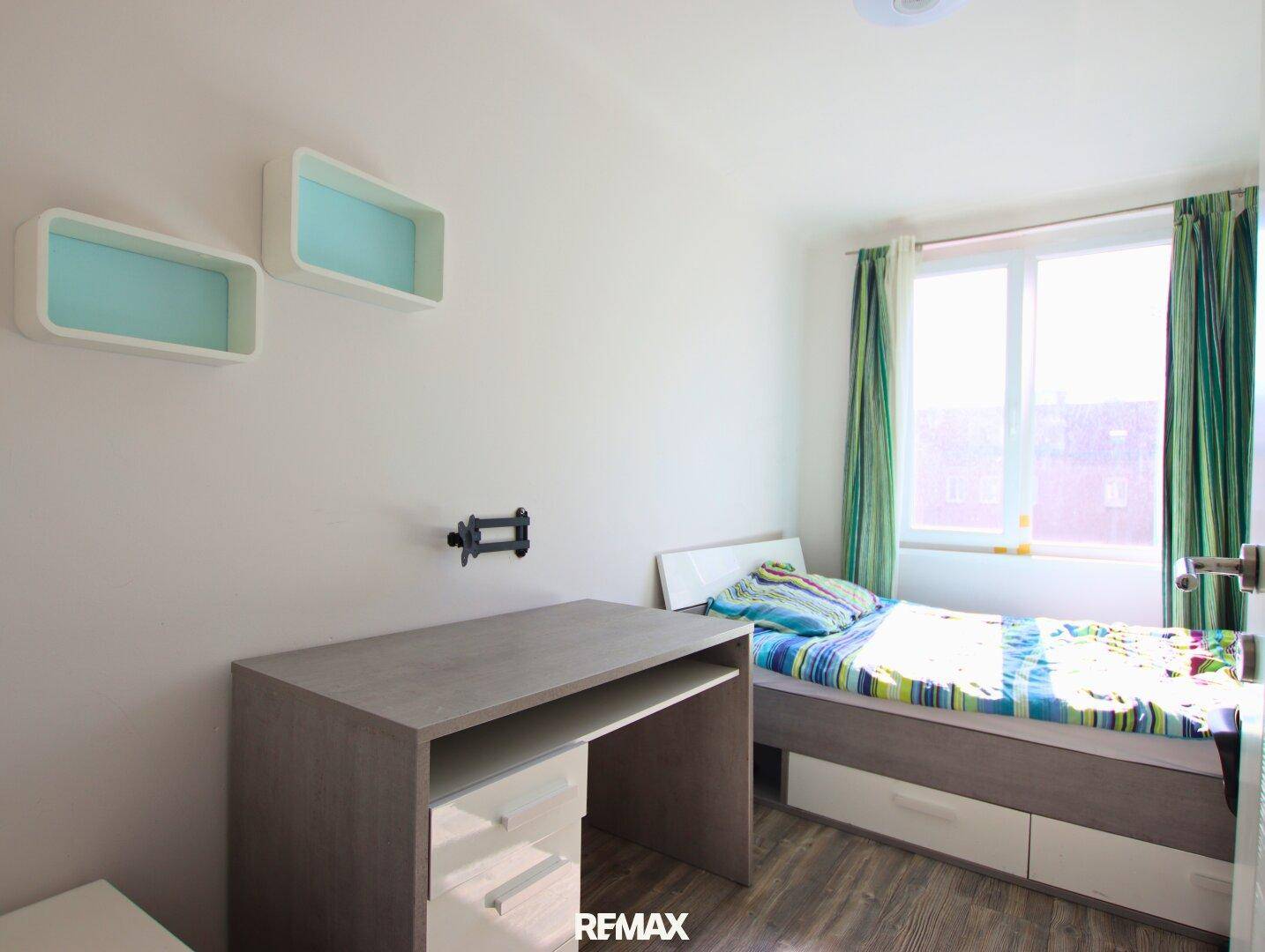Helles Kinder- oder Gästezimmer mit Einzelbett, Schreibtisch und Laminatboden, freundlich gestaltet.