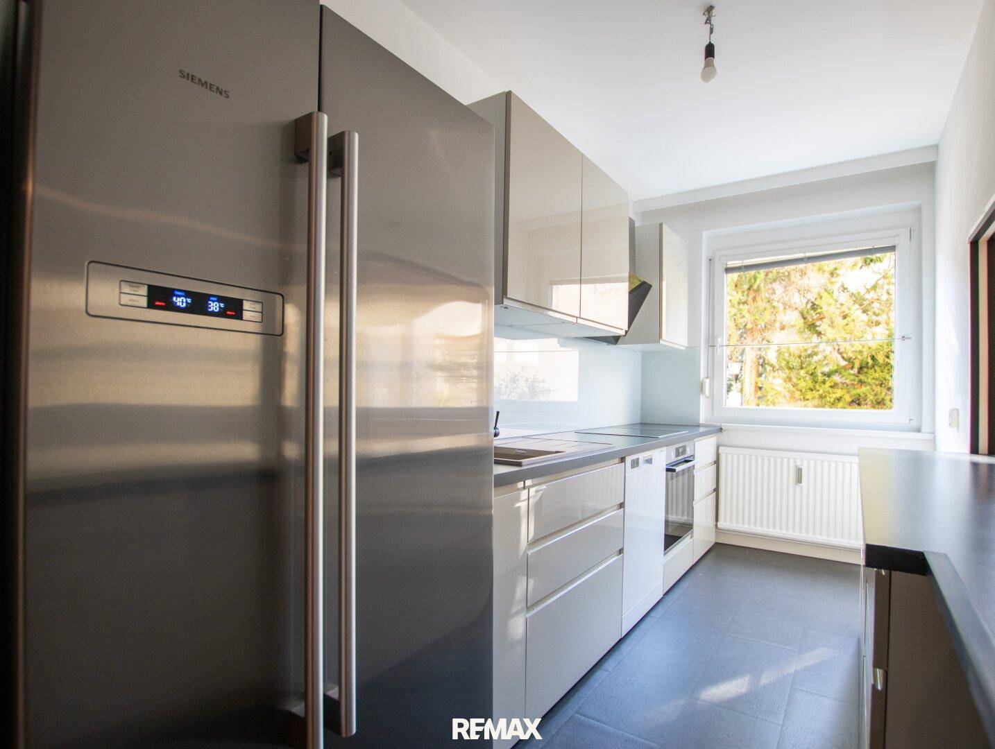Funktionale Küche mit weißen Hochglanzschränken, großem Siemens Kühlschrank und Fenster mit Tageslicht.