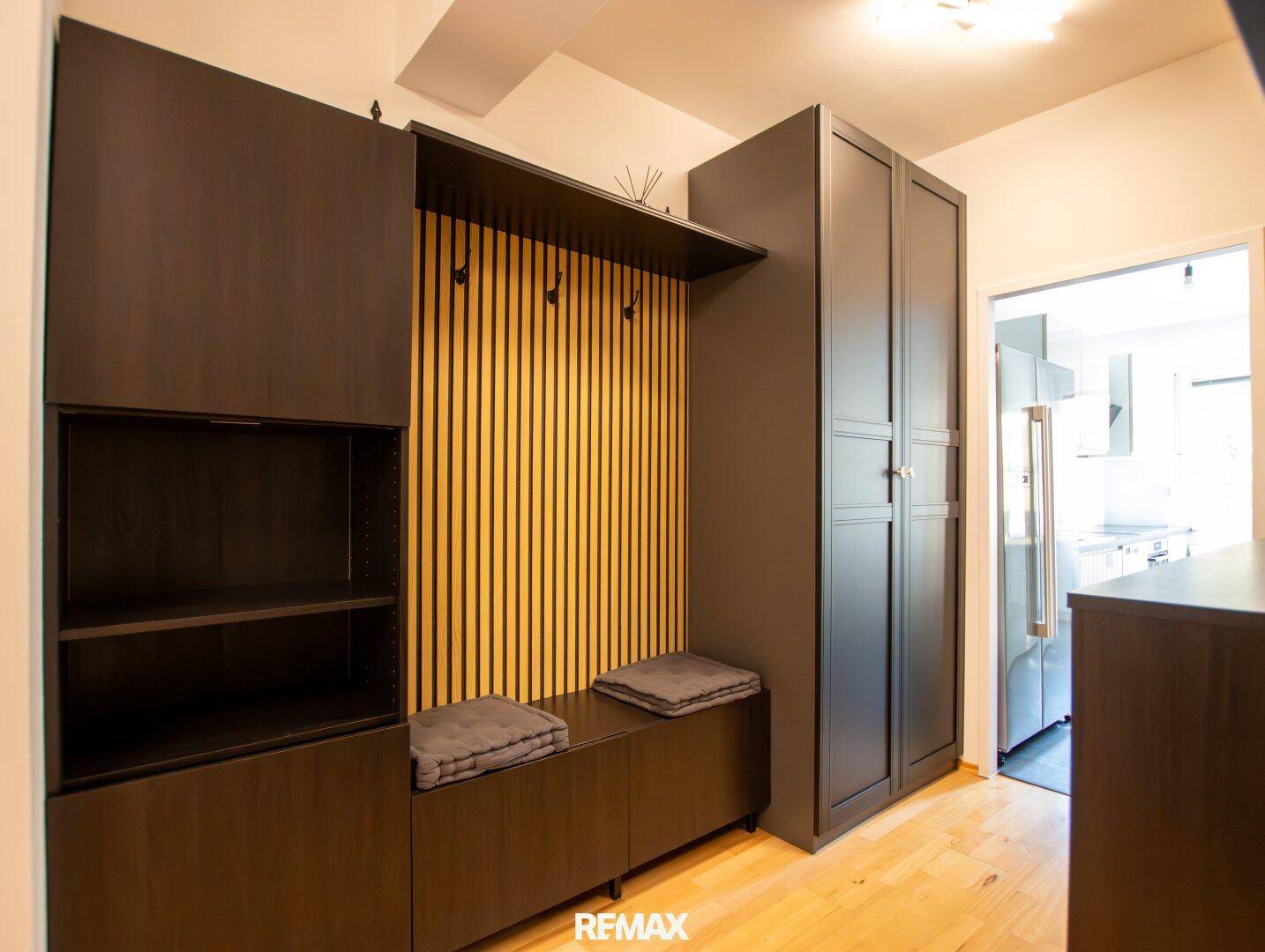 Moderner Flur mit dunklen Einbaumöbeln, Garderobe und Sitzbank, die zum Eingangsbereich einlädt.