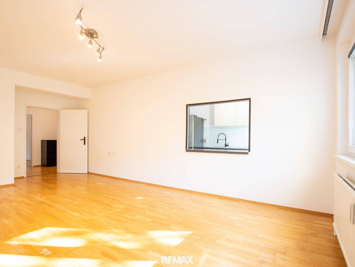 Geräumiges Wohnzimmer mit Parkettboden und einem praktischen Durchgangsfenster zur angrenzenden Küche.