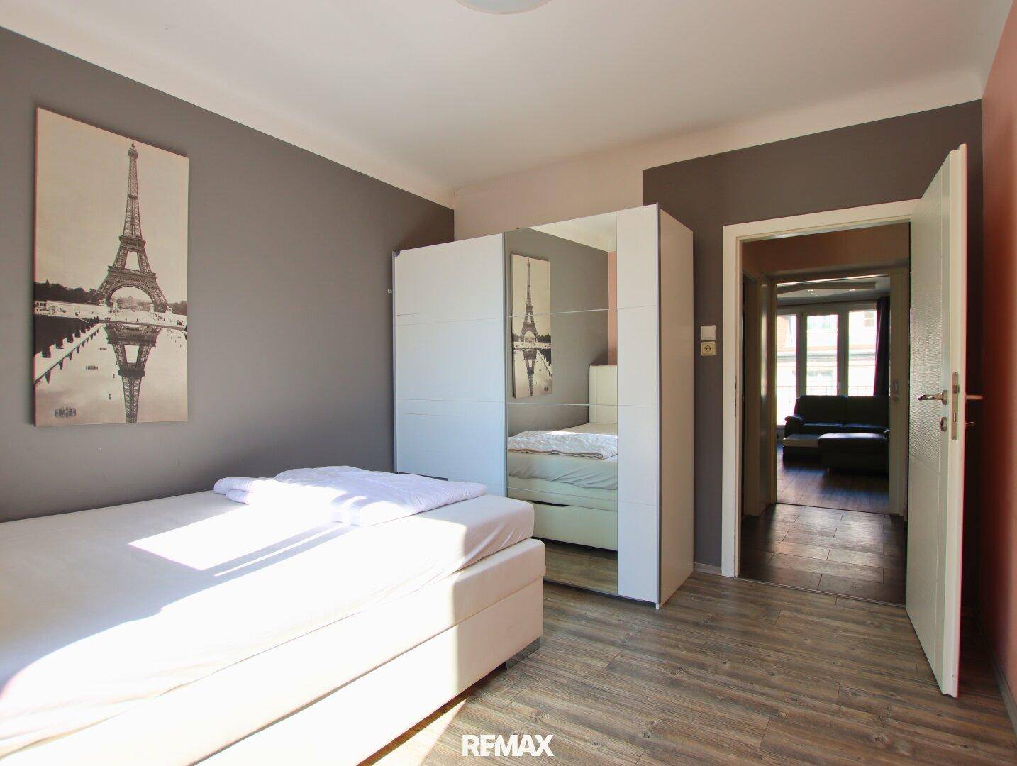 Helles Schlafzimmer mit Einzelbett, großem Spiegelschrank und Blick in den angrenzenden Raum.
