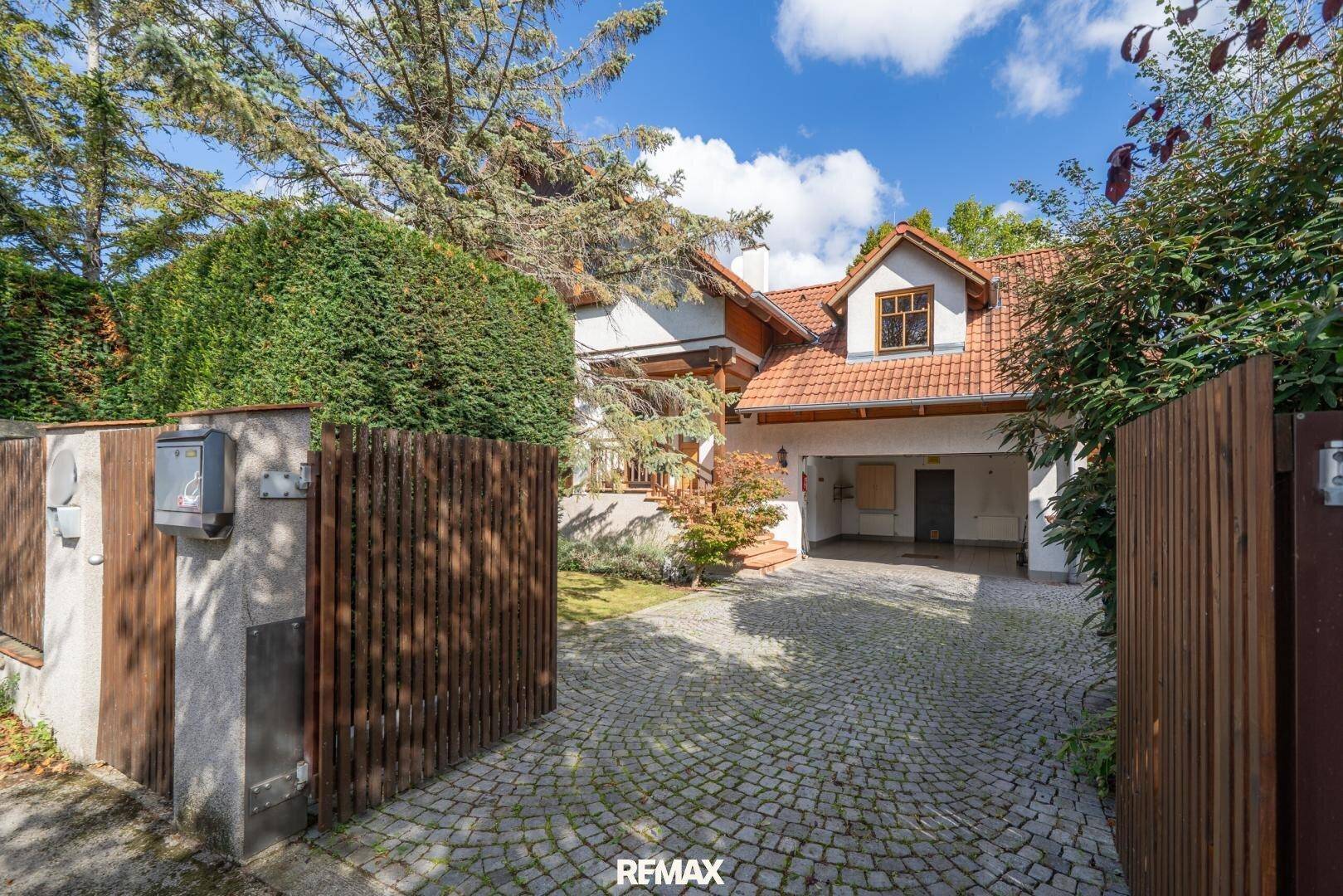 Einfahrt zum Haus mit Kopfsteinpflaster, Garage und üppiger Begrünung im Vorgarten.