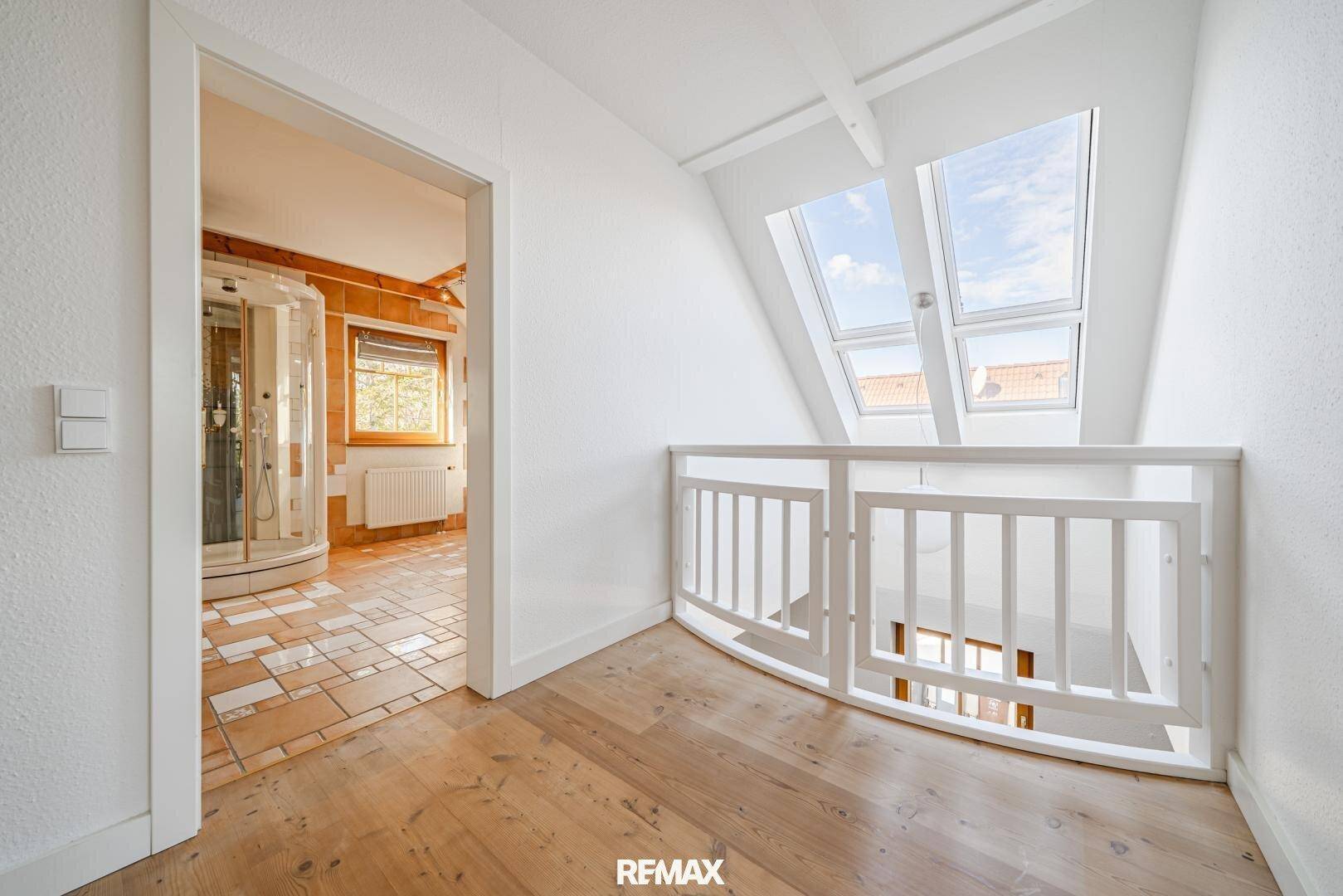 Heller Flur im Obergeschoss mit Dachfenstern und Blick in ein Badezimmer mit Dusche.