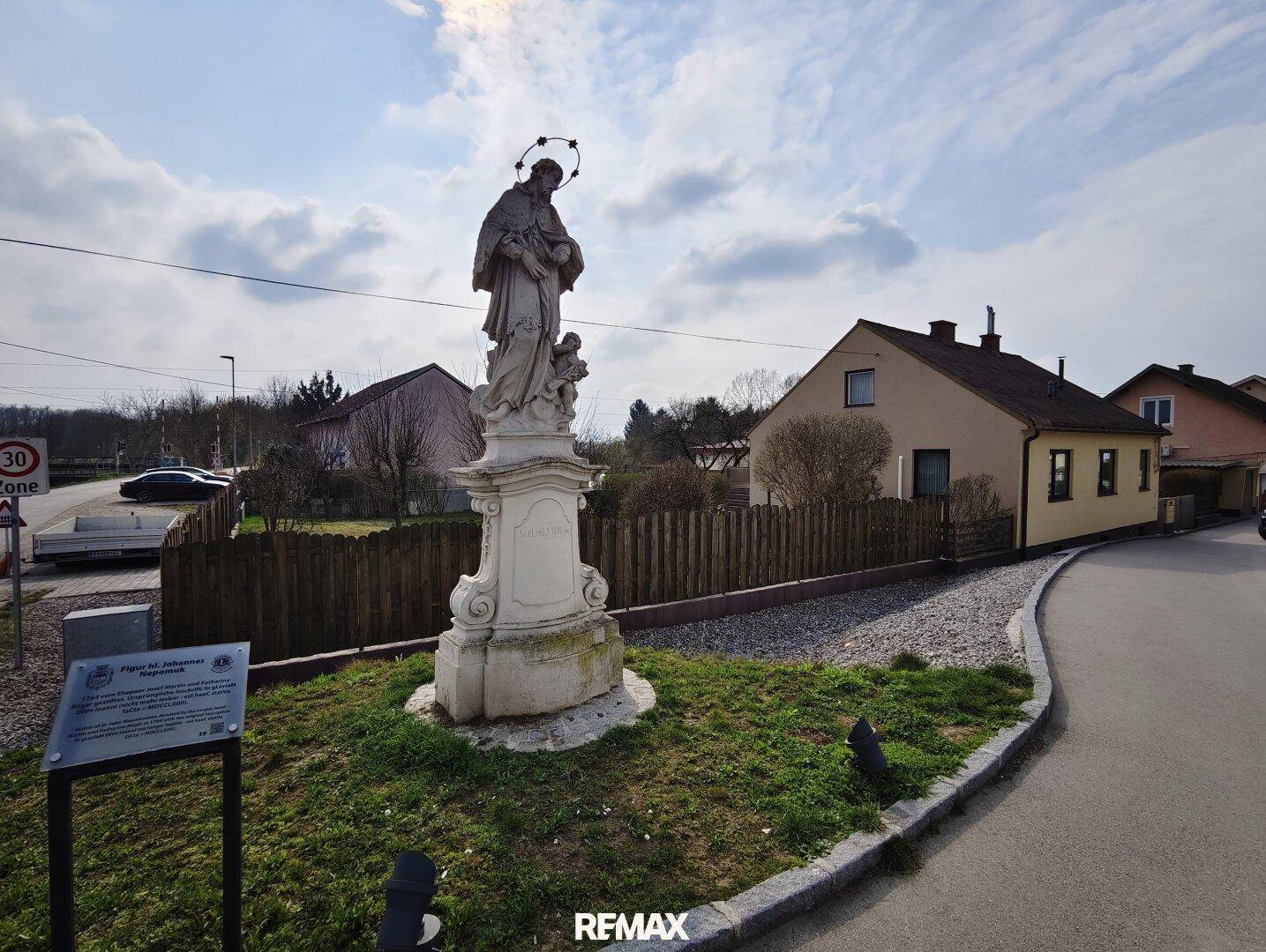 Ruhige Wohngegend mit einer Statue am Straßenrand und Einfamilienhäusern im Hintergrund.