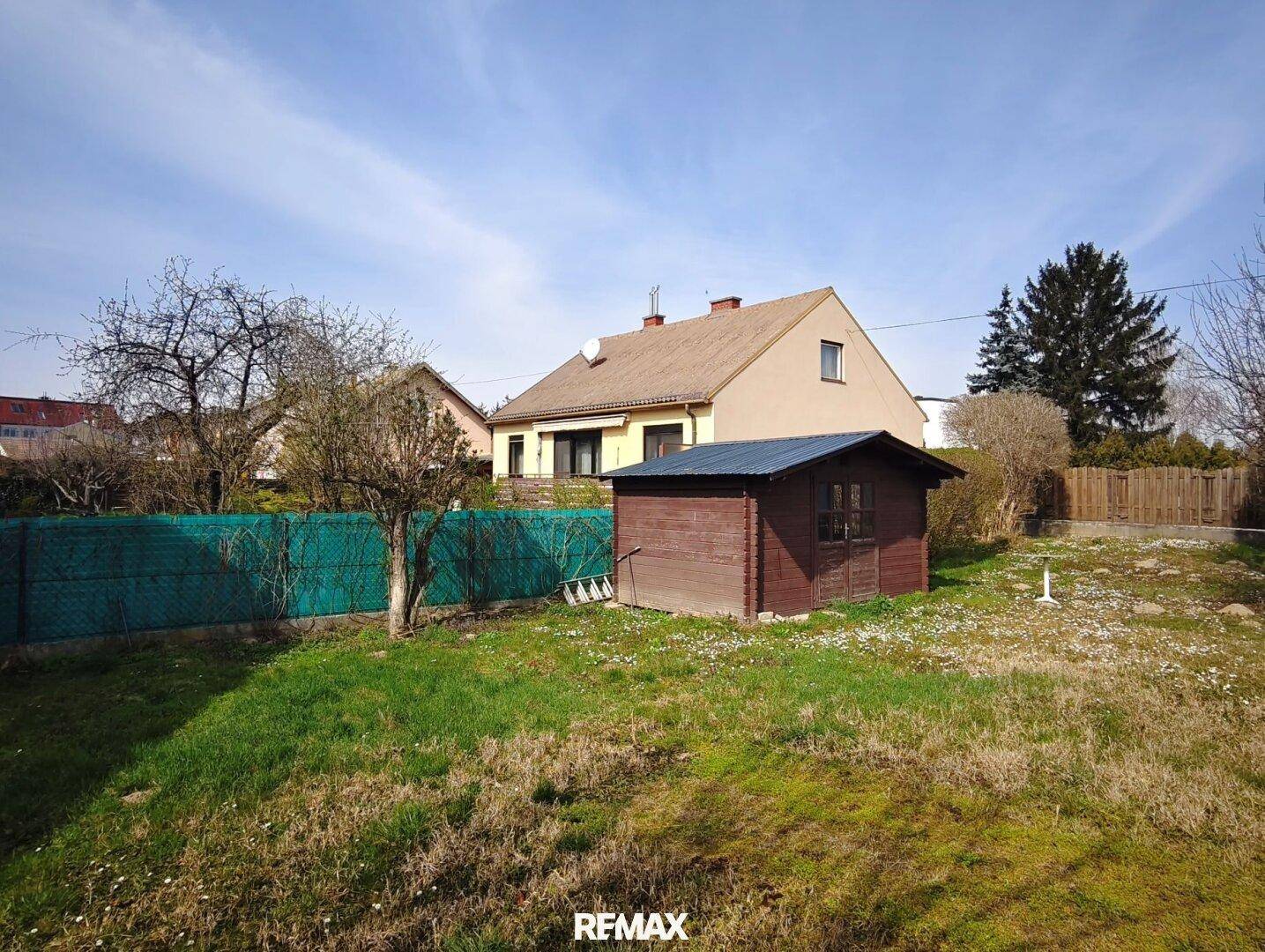 Gepflegter Gartenbereich mit Rasen, einem kleinen Holzschuppen und grüner Umzäunung.
