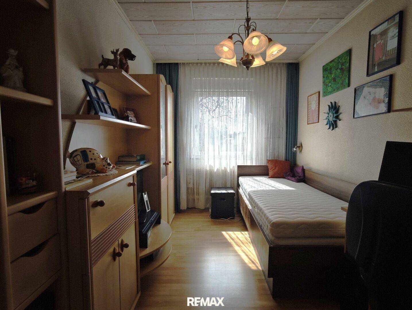 Helles Kinder- oder Gästezimmer mit Holzfußboden, Einzelbett und praktischen Regalen.
