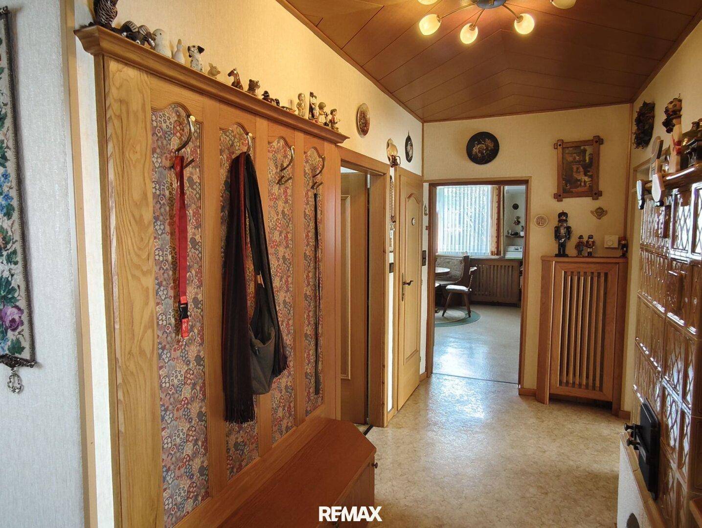 Eingangsbereich mit Garderobe, Holzvertäfelung und traditionellem Kachelofen im Hintergrund.
