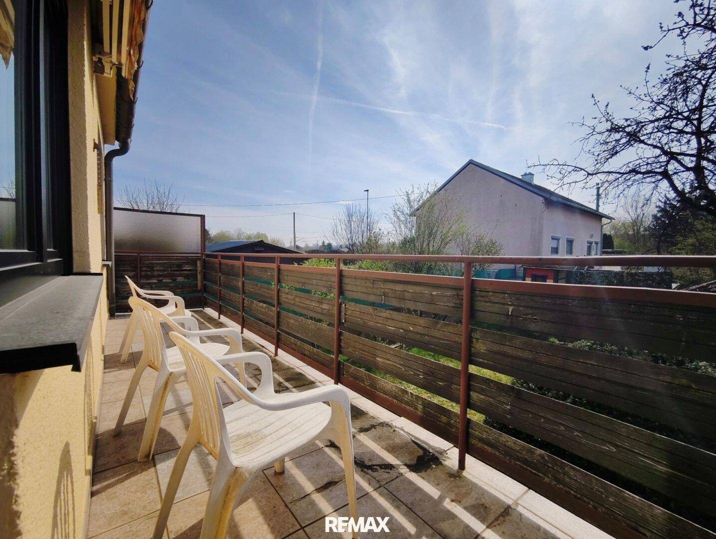Sonniger Balkon mit einfachen Gartenstühlen und Blick auf die Umgebung.