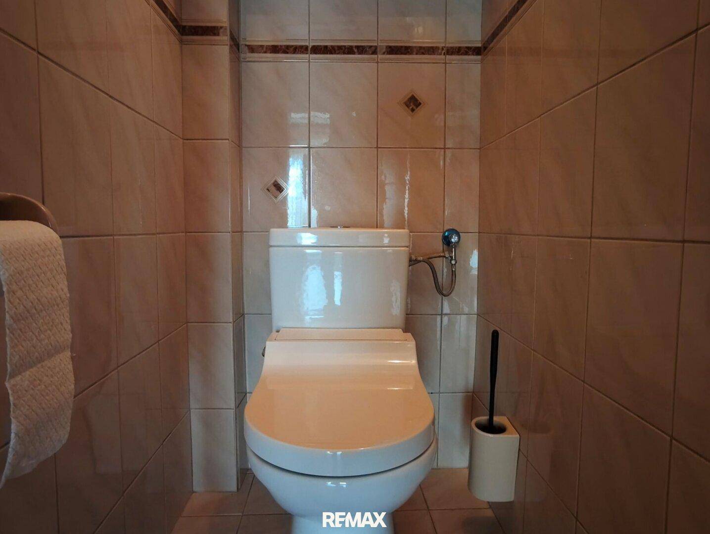 Separate Toilette mit hellen Fliesen an Wänden und Boden, funktional und sauber.