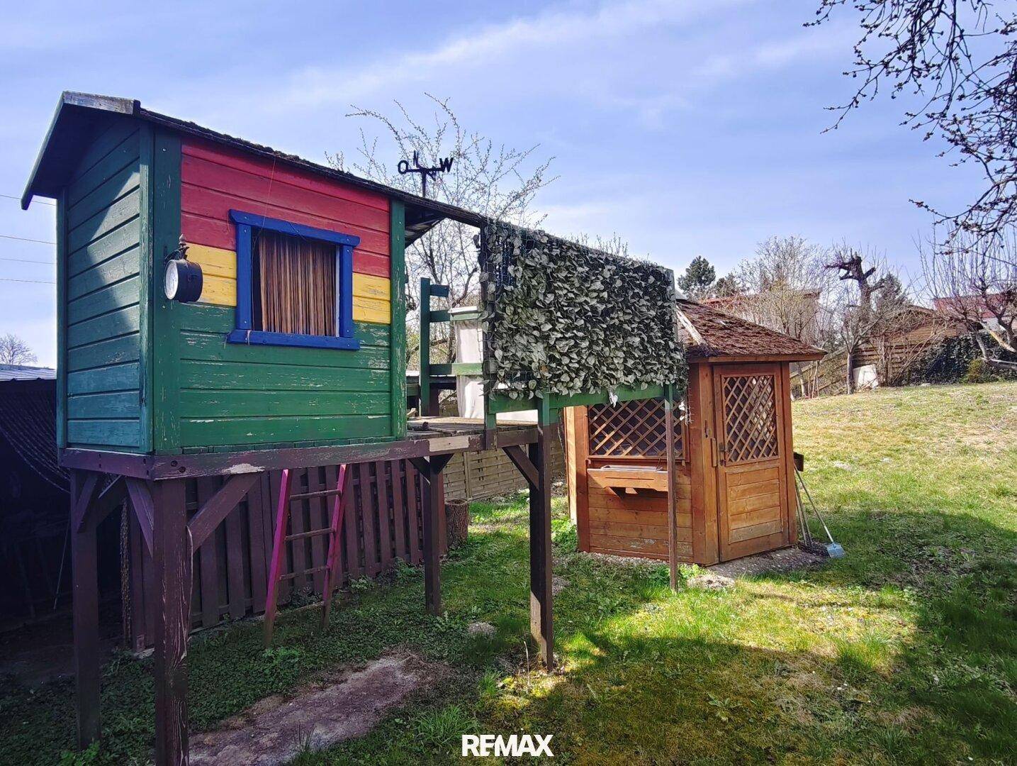 Großer Garten mit farbenfrohem Baumhaus und einem kleinen Holzpavillon für Kinder.