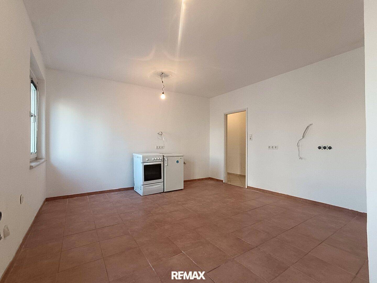 Leerer Küchenbereich mit Terrakotta-Fliesenboden, Fenster und grundlegenden Geräten.