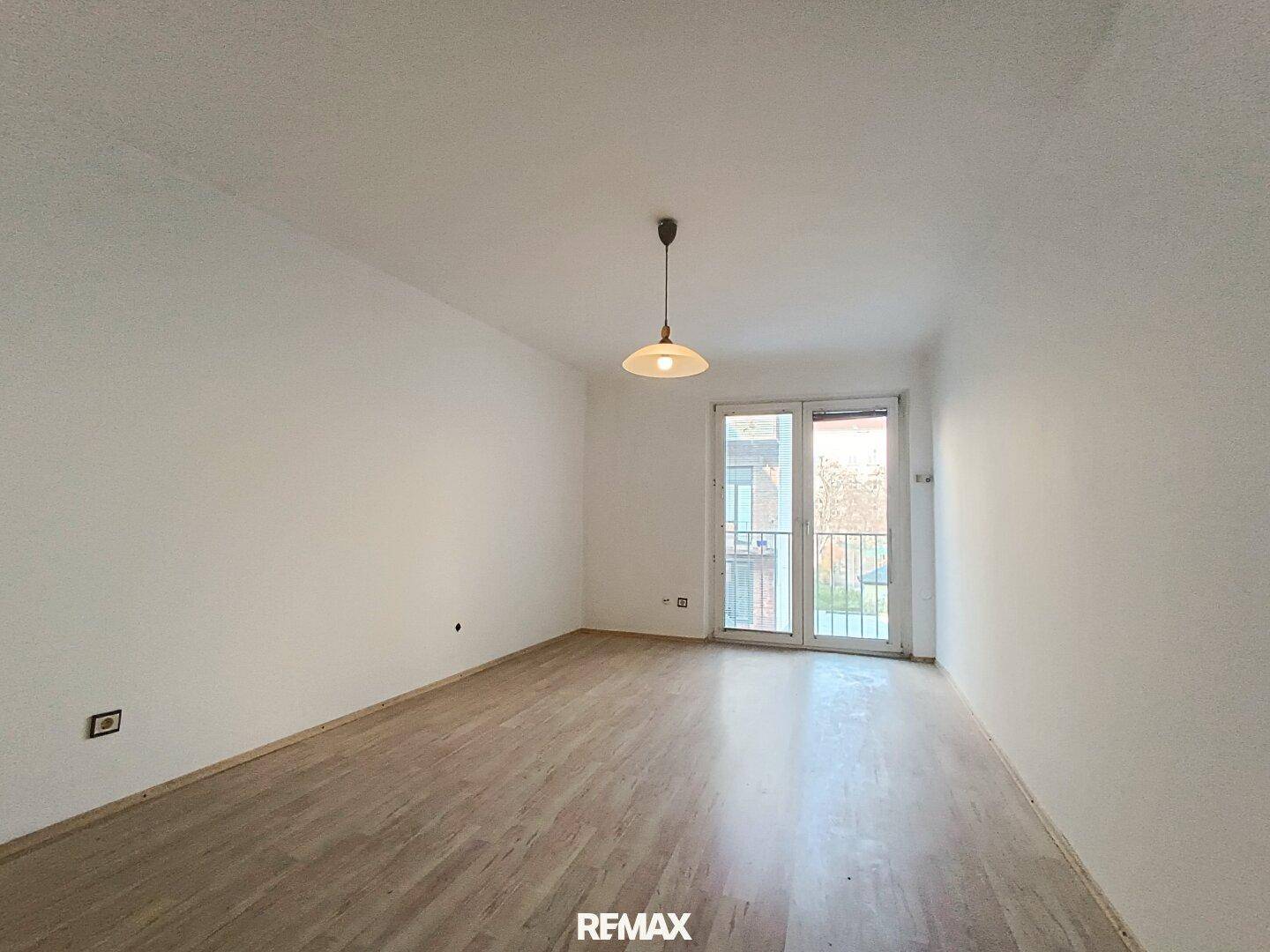Heller Raum mit Laminatboden, weißen Wänden und Zugang zu einem französischen Balkon.