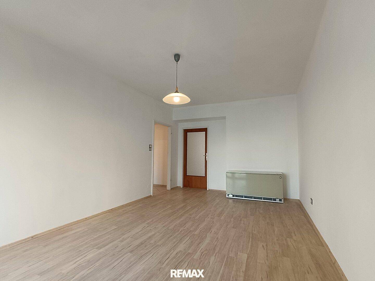 Leerer Raum mit Laminatboden, weißen Wänden und einem Heizkörper.