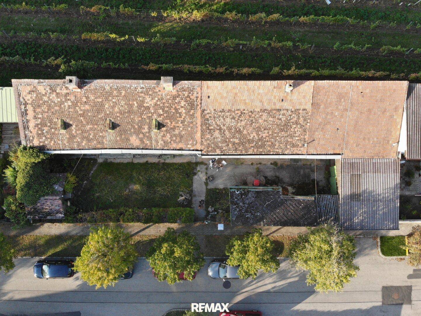 Draufsicht auf das Anwesen mit langem Gebäude, Gartenbereich und angrenzenden Weinbergen.