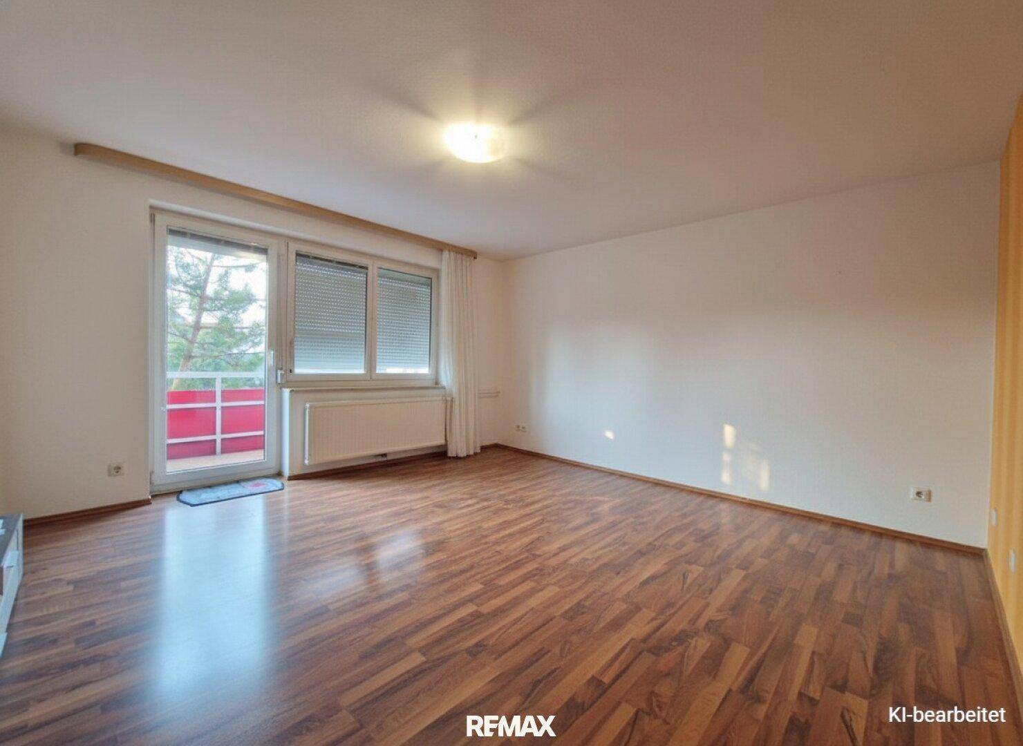 Helles, leeres Wohnzimmer mit Laminatboden und Balkonzugang nach Renovierung.