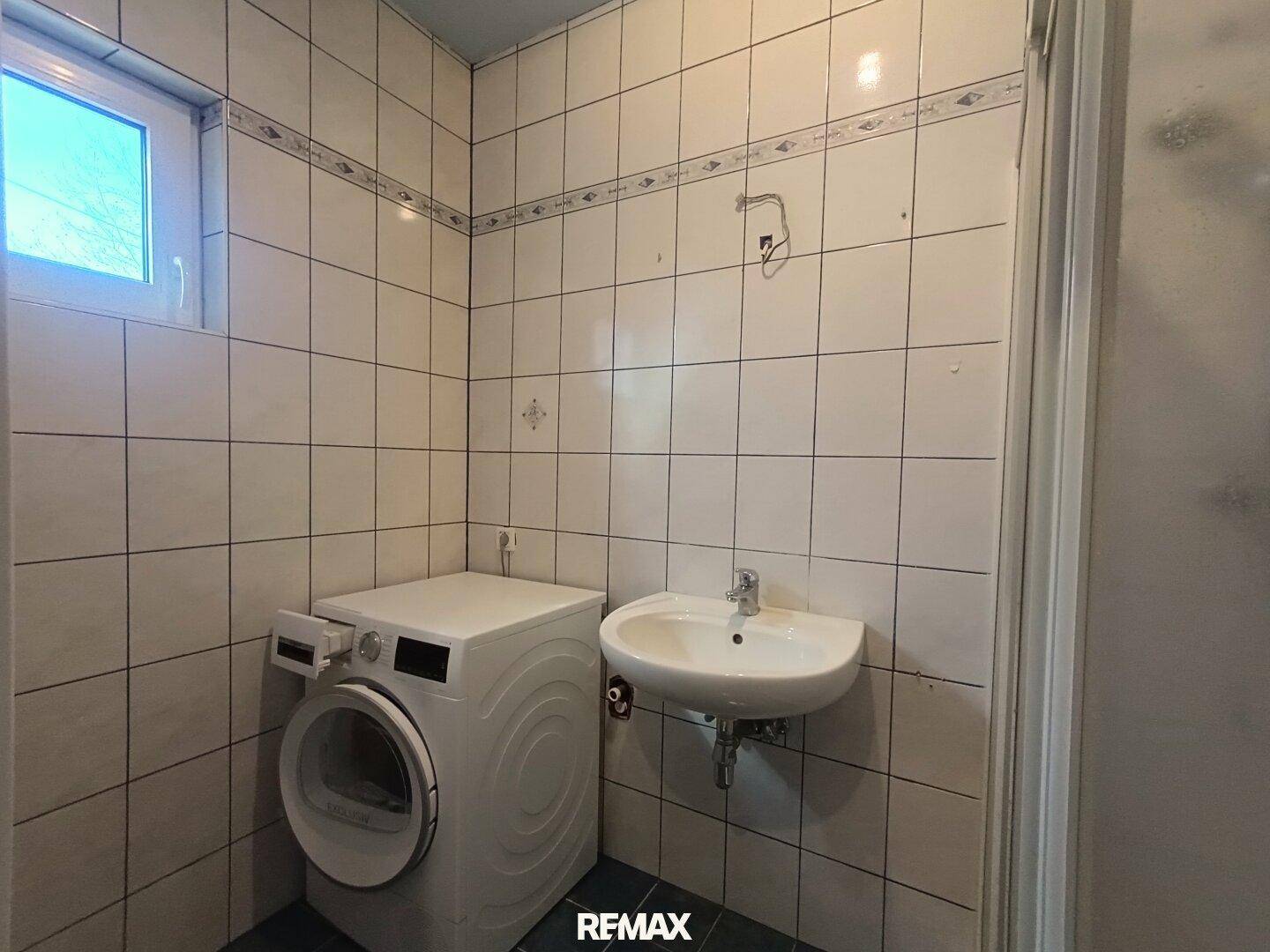 Helles Badezimmer mit Waschbecken, Waschmaschine und Fenster für natürliche Belüftung, praktisch gestaltet.