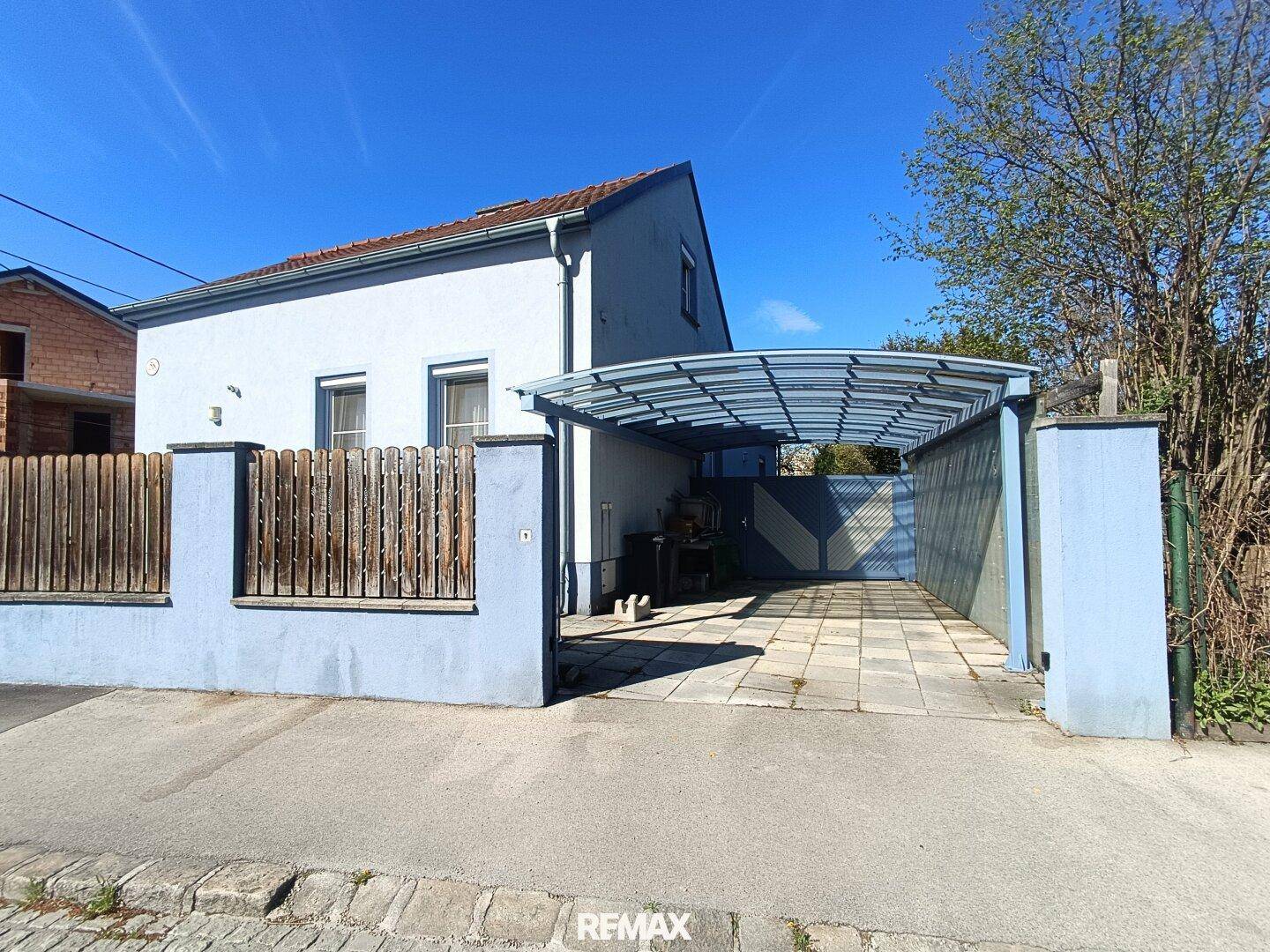 Seitenansicht des Hauses mit überdachtem Carport und gepflasterter Einfahrt an einem sonnigen Tag.