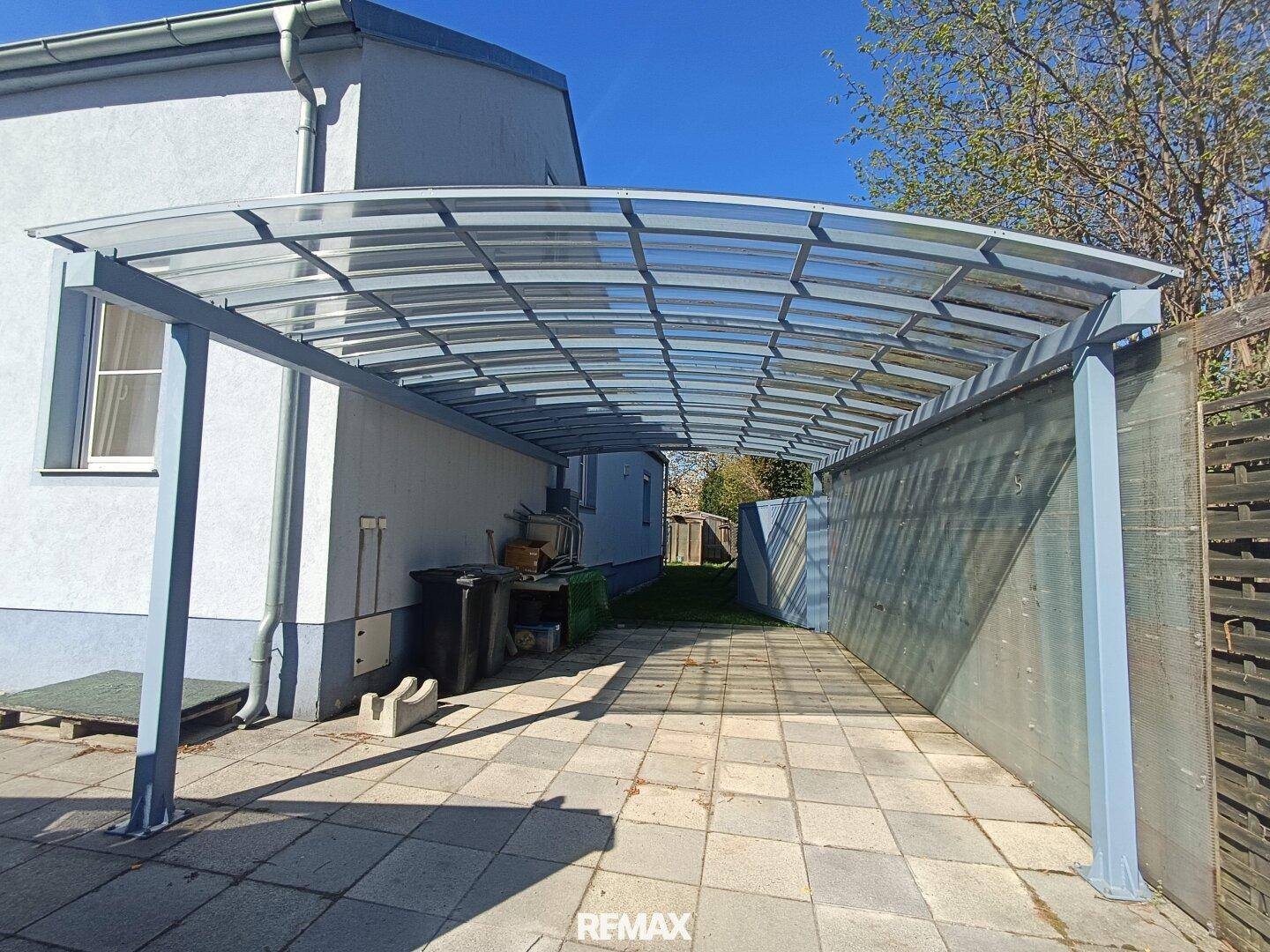 Langer überdachter Carport mit Metallkonstruktion und gepflastertem Boden, bietet Schutz für Fahrzeuge.