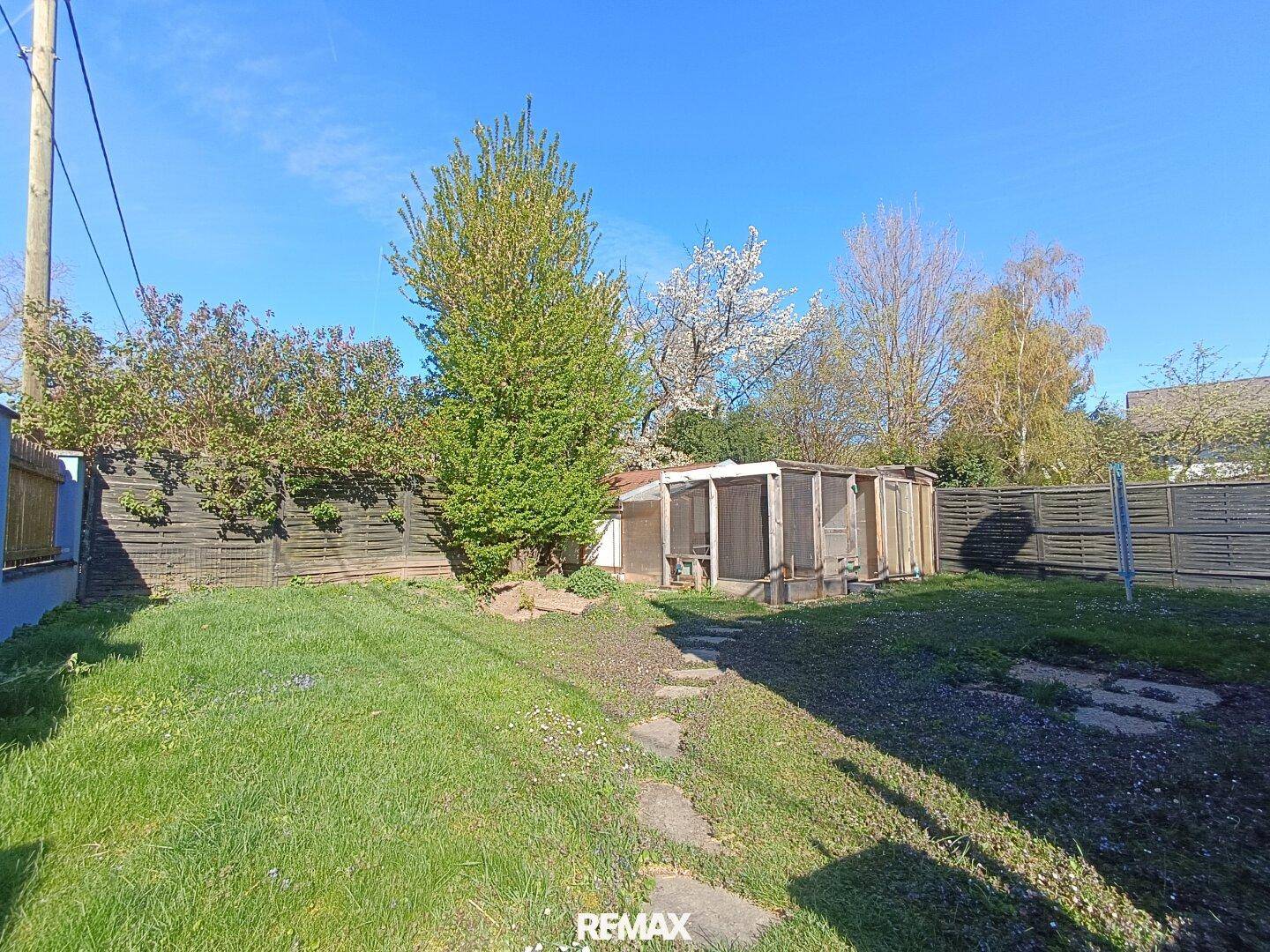 Großer Gartenbereich mit Rasenfläche, Bäumen und einem Gartenhaus im Hintergrund, ideal zum Entspannen.