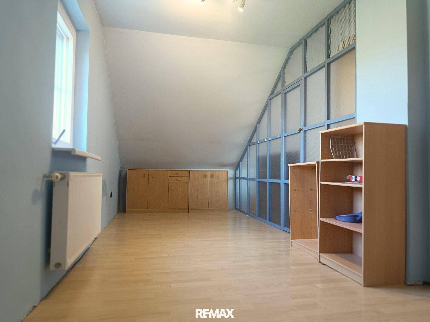 Helles Dachgeschosszimmer mit Dachschräge, Laminatboden und integrierten Holzschränken für Stauraum.