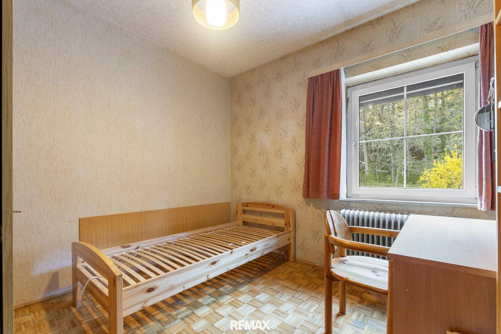 Kleines Schlafzimmer mit Einzelbett, Holzdecke und Fenster zum Wald.