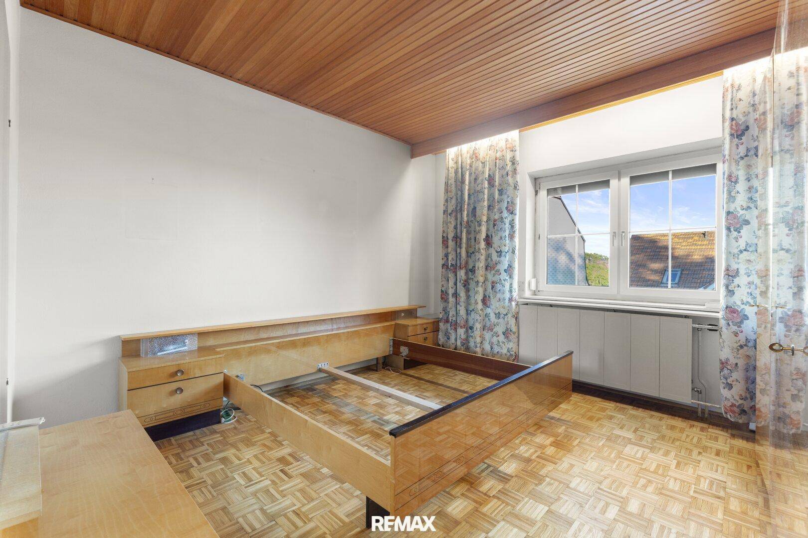 Schlafzimmer mit Holzbettrahmen, Holzdecke und Blick ins Grüne.