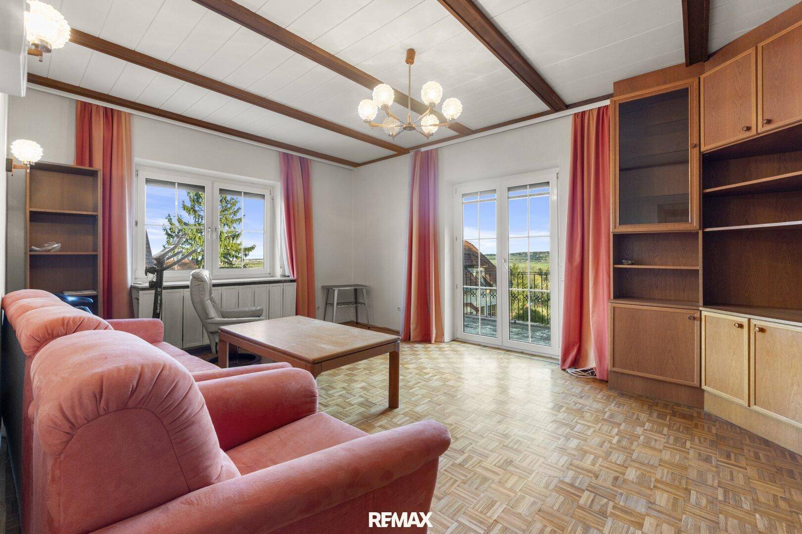 Helles Wohnzimmer mit Parkettboden, Holzbalken und Zugang zum Balkon.