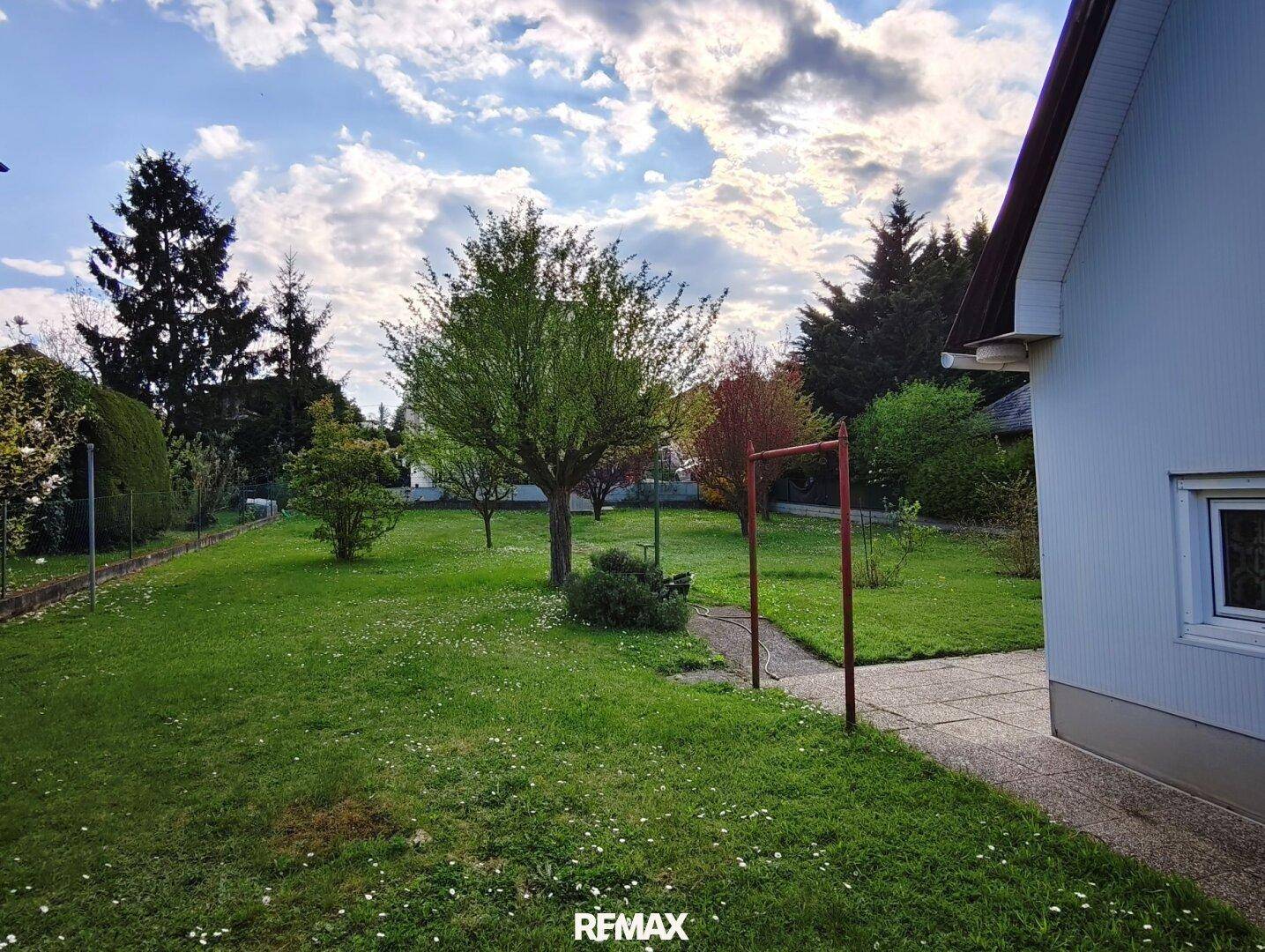 Großer, gepflegter Garten mit Rasenfläche und Bäumen neben dem Haus unter bewölktem Himmel.