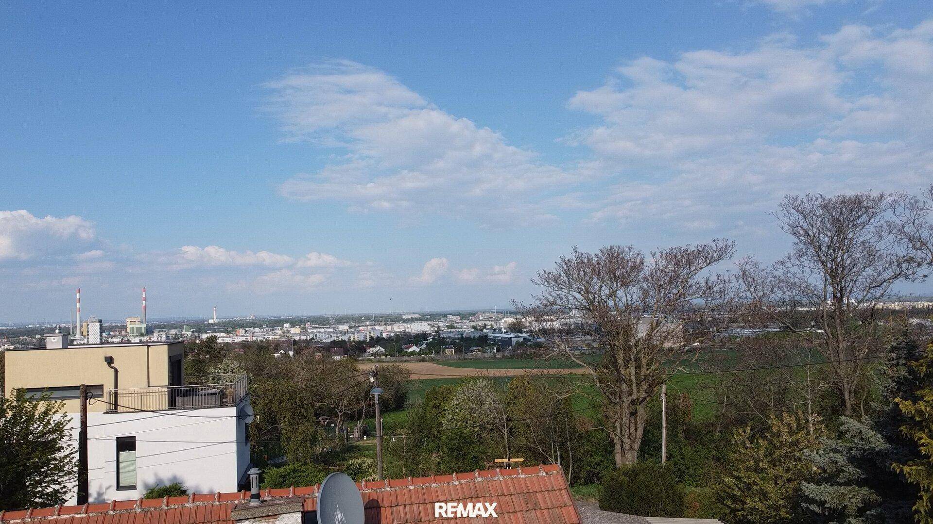 Weitblick über die Stadt mit Feldern und Bäumen unter blauem Himmel und moderner Architektur.