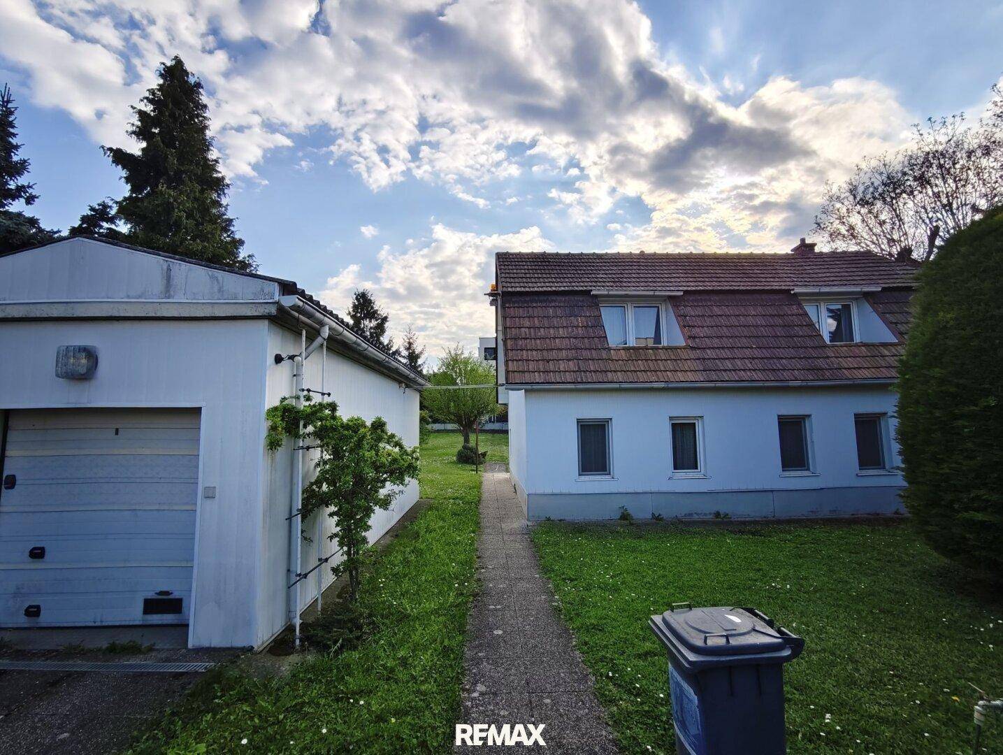 Seitenansicht des Hauses mit Satteldach und einem separaten Garagengebäude im Garten.