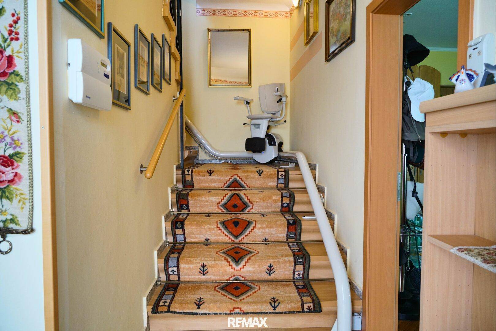 Treppenhaus mit Teppichläufer und einem Treppenlift für Barrierefreiheit.