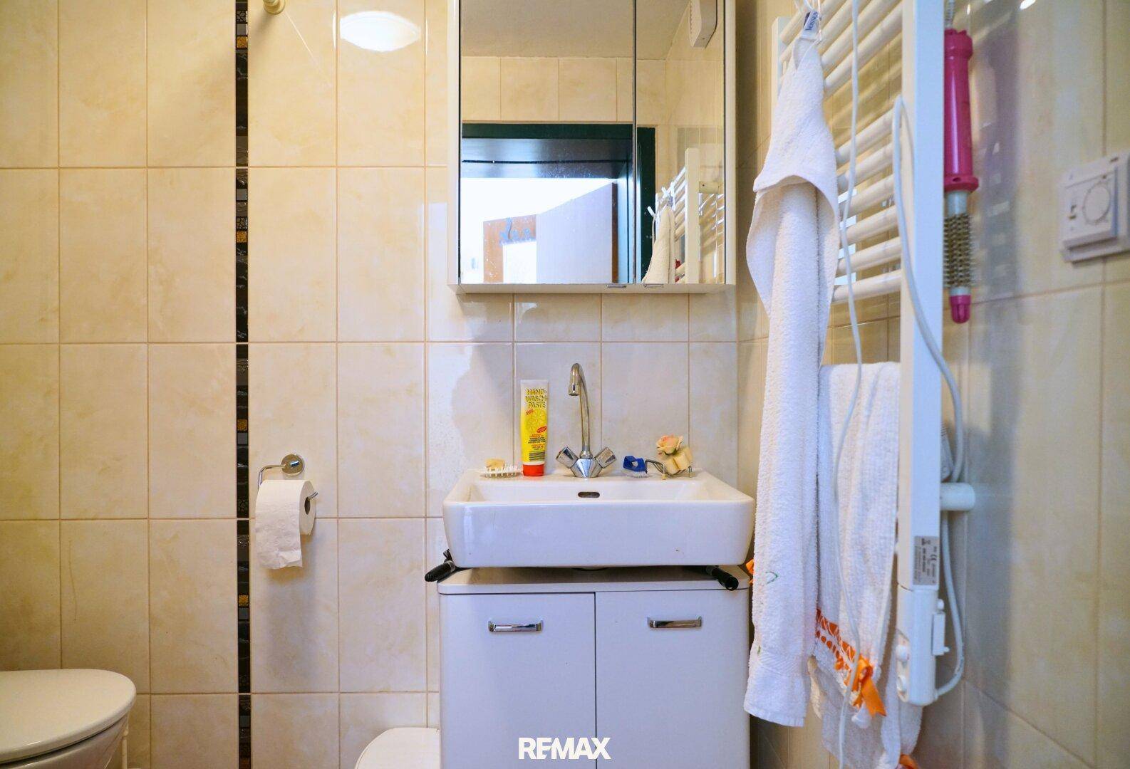 Kleines Badezimmer mit Waschbecken, Toilette und beheiztem Handtuchhalter.