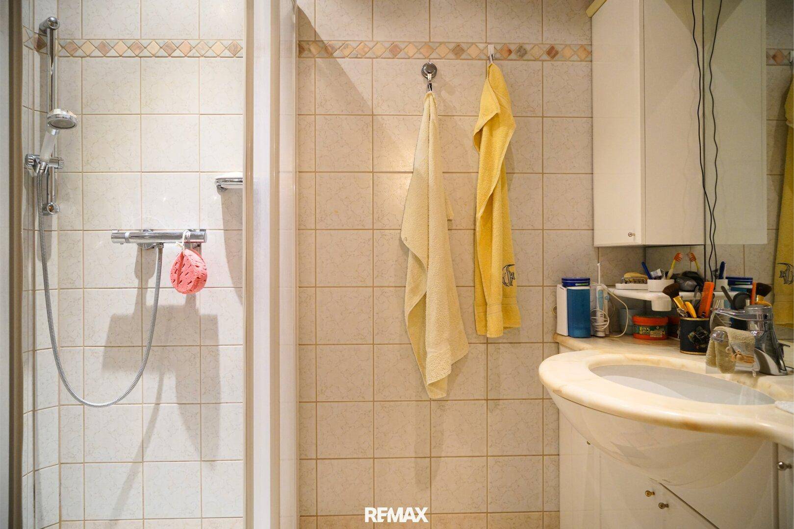 Kleines Badezimmer mit Duschkabine, Waschbecken und hellen Fliesen.