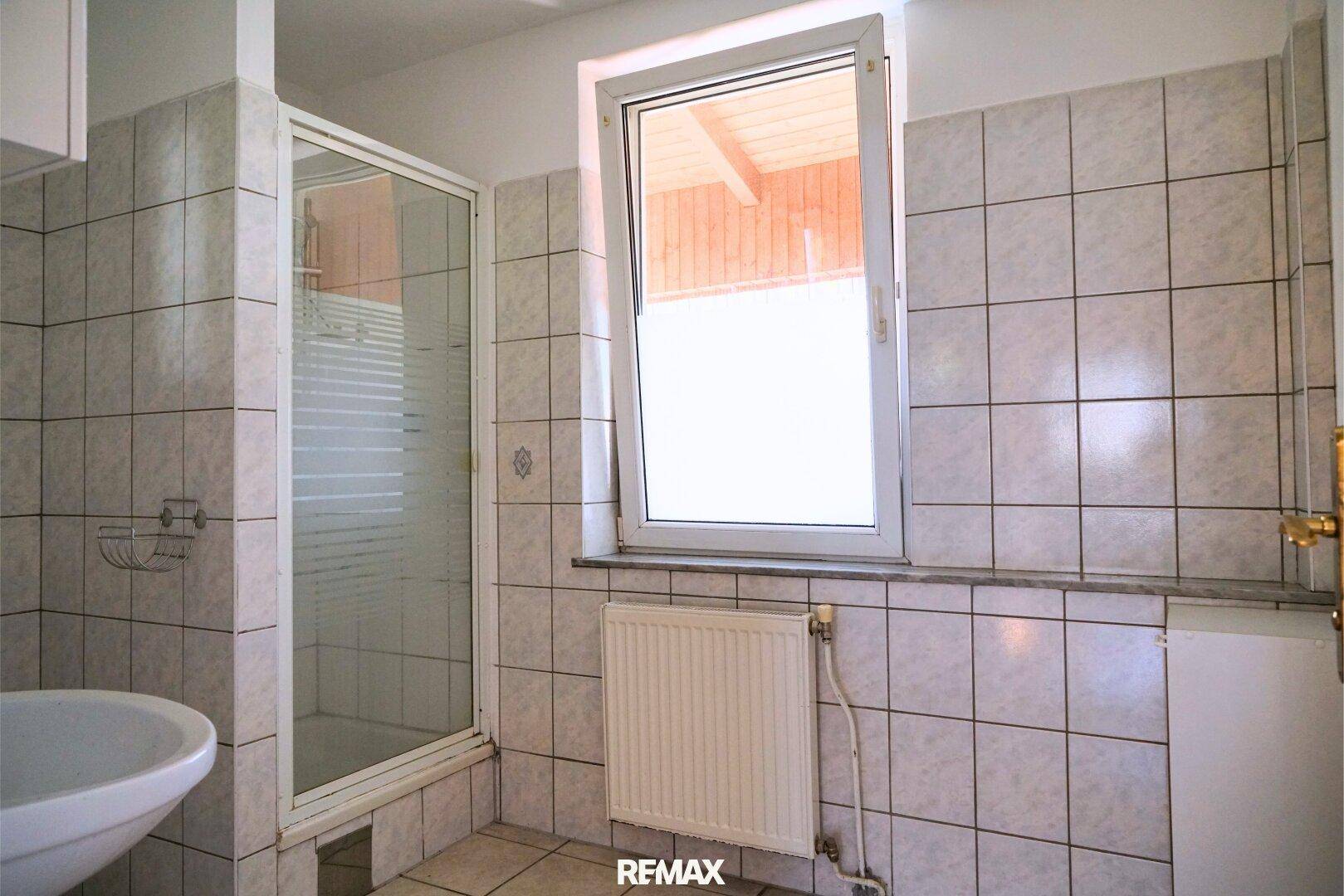 Badezimmer mit Duschkabine, Waschbecken und Fenster für Tageslicht.