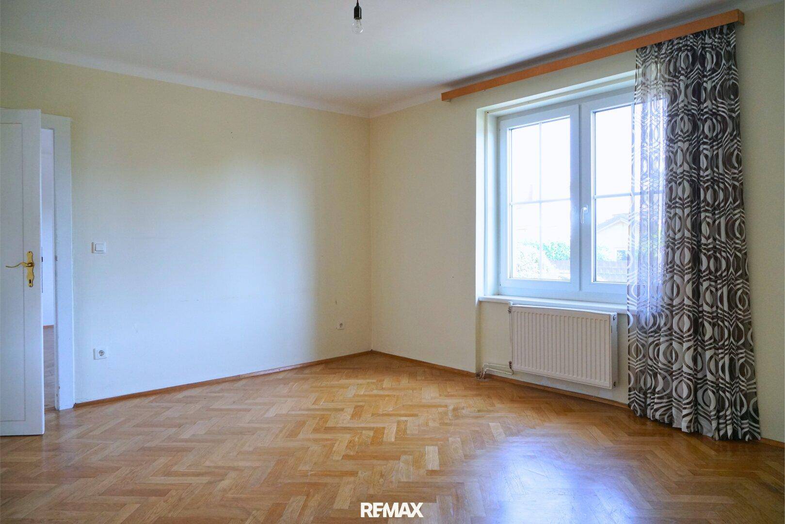 Helles Zimmer mit Fischgrätparkett, weißen Wänden und großem Fenster.
