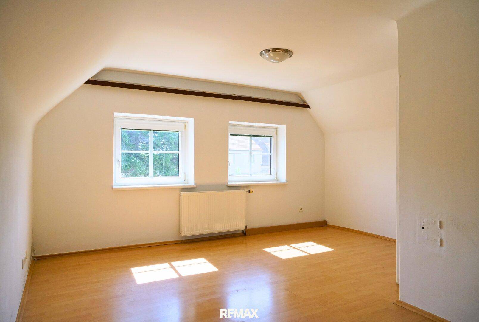 Helles Dachzimmer mit Holzboden, weißen Wänden und zwei Fenstern.
